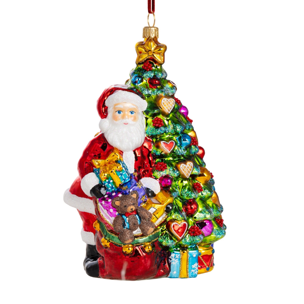 Père Noël en verre soufflé rouge tenant des cadeaux au pied d'un sapin décoré
