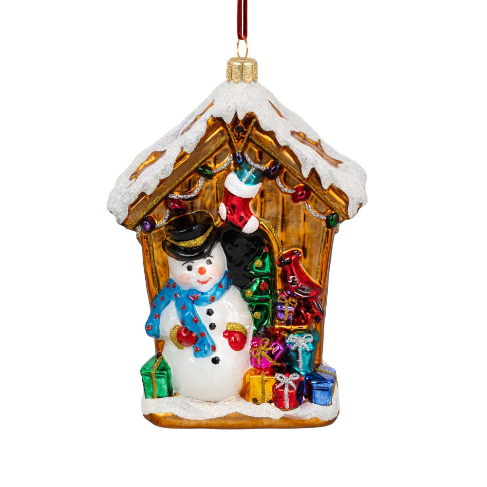 Bonhomme de neige en verre soufflé devant une maison dorée couverte de neige et cadeaux