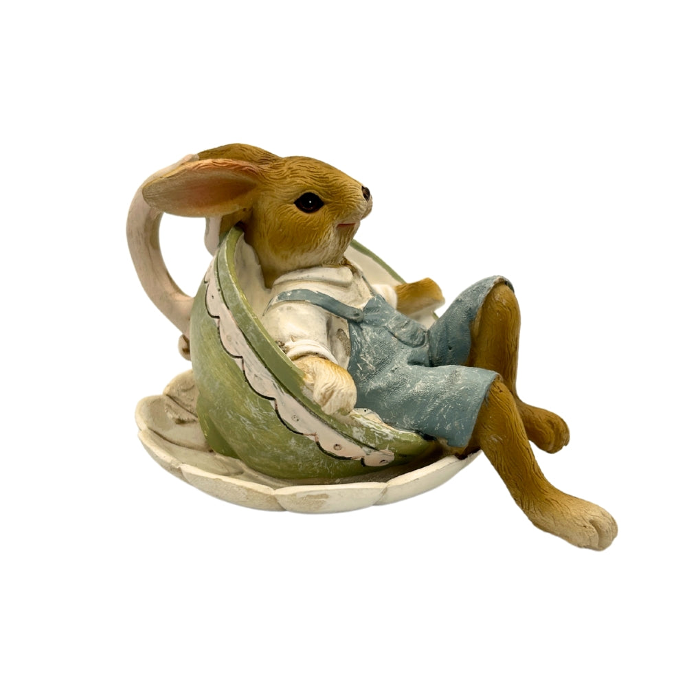 Lapin décoratif assis dans une tasse verte sur soucoupe, vêtements peints à la main