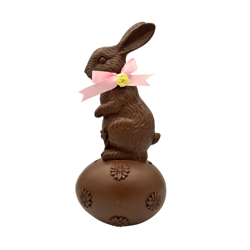 Lapin en chocolat décoratif sur un oeuf brun avec nœud rose et fleur jaune
