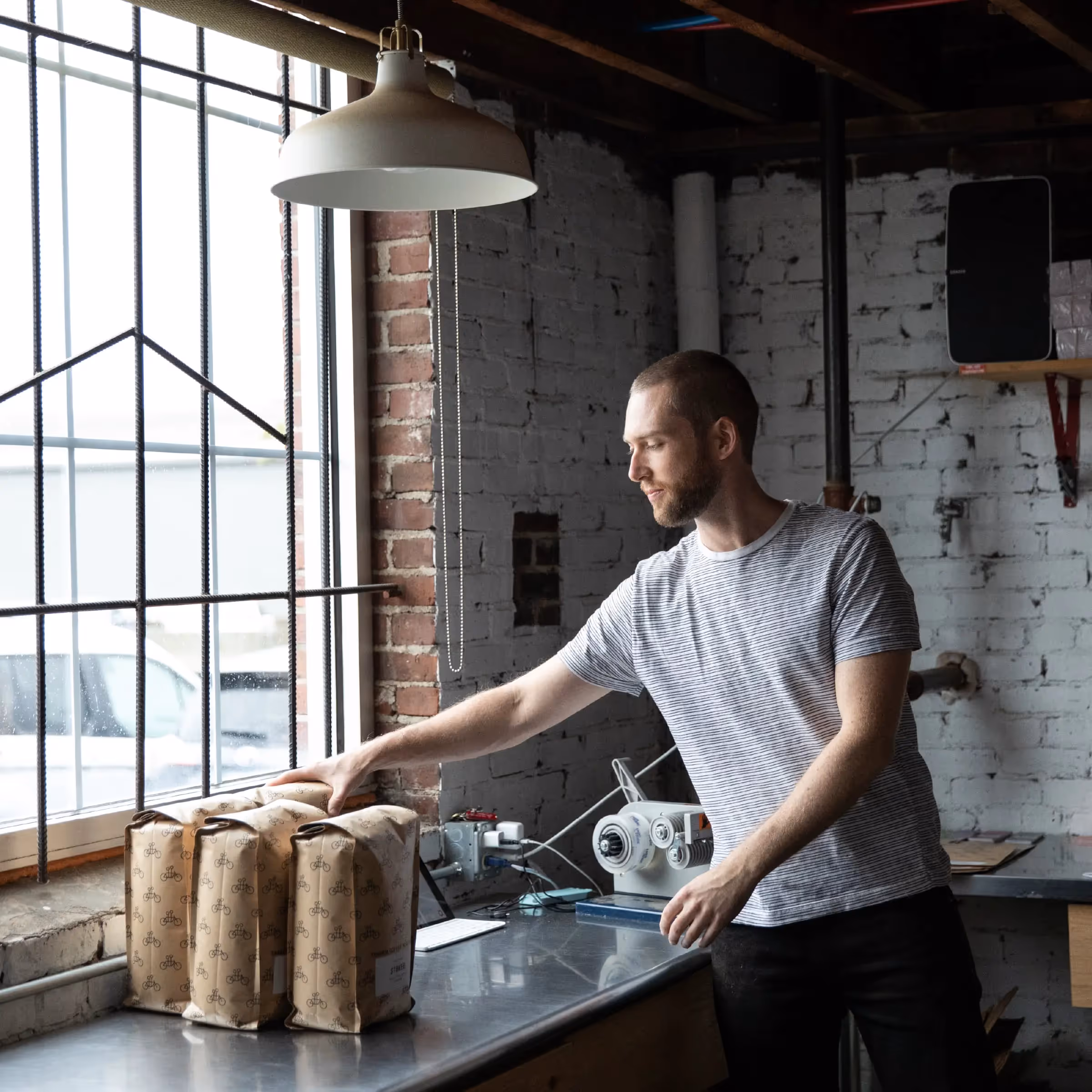 Worker packaging bags near industrial window in rustic workshop