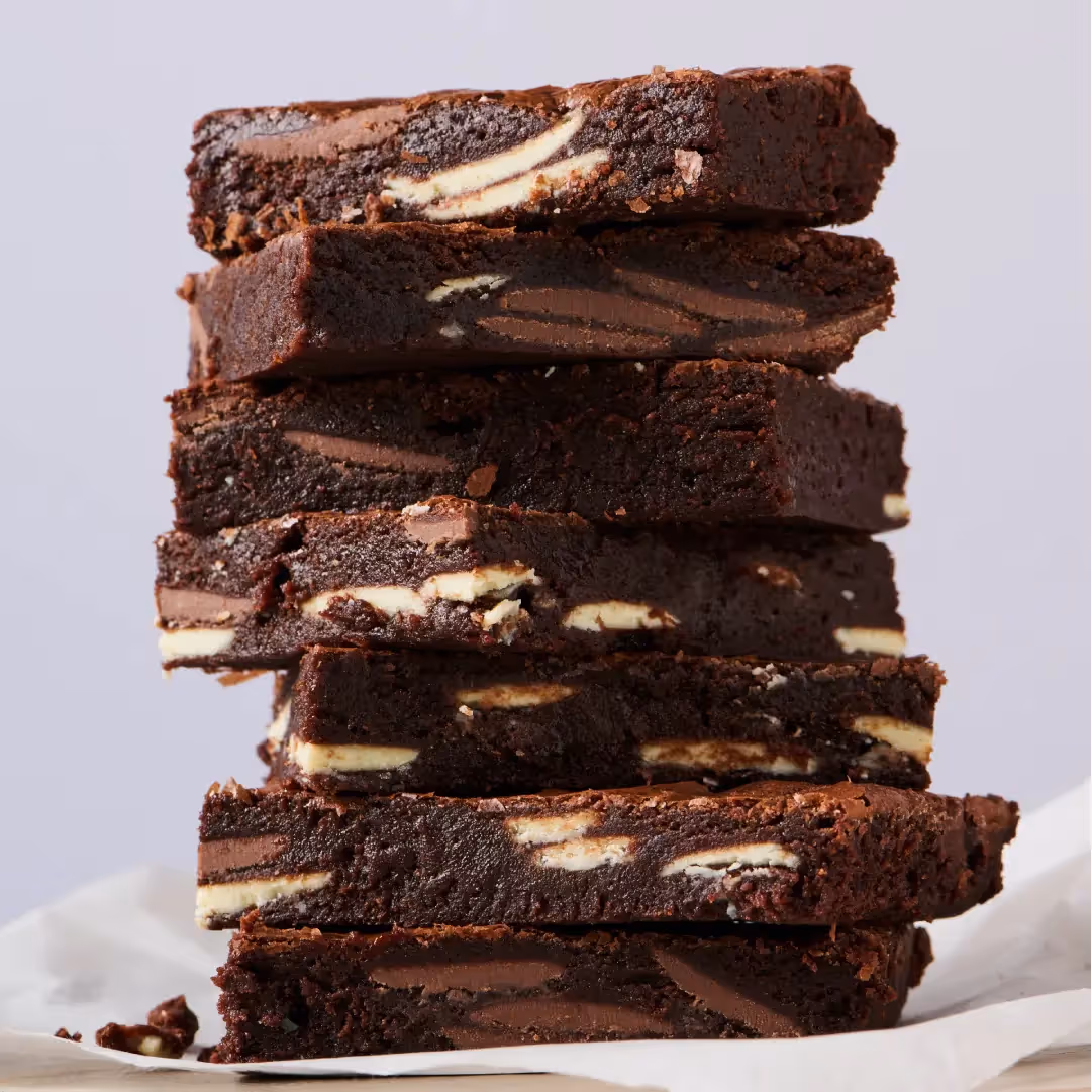 Stack of layered chocolate brownies with cream filling on white surface