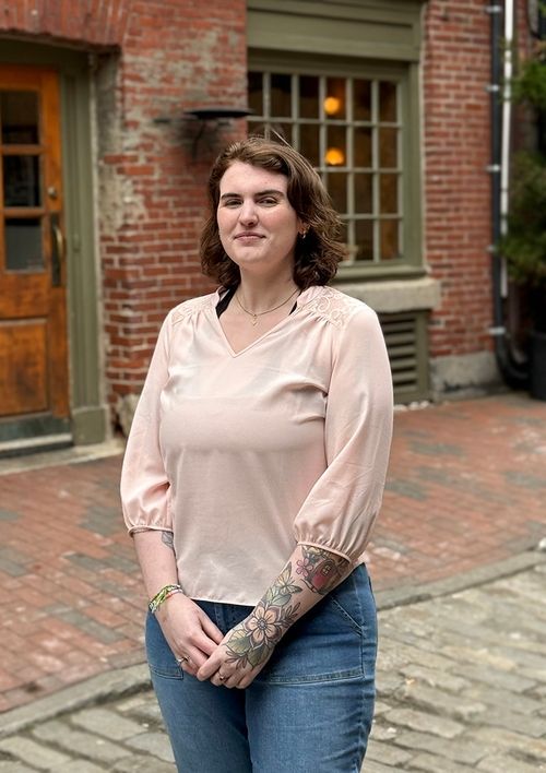 A person standing on a cobblestone street with brick buildings in the background.