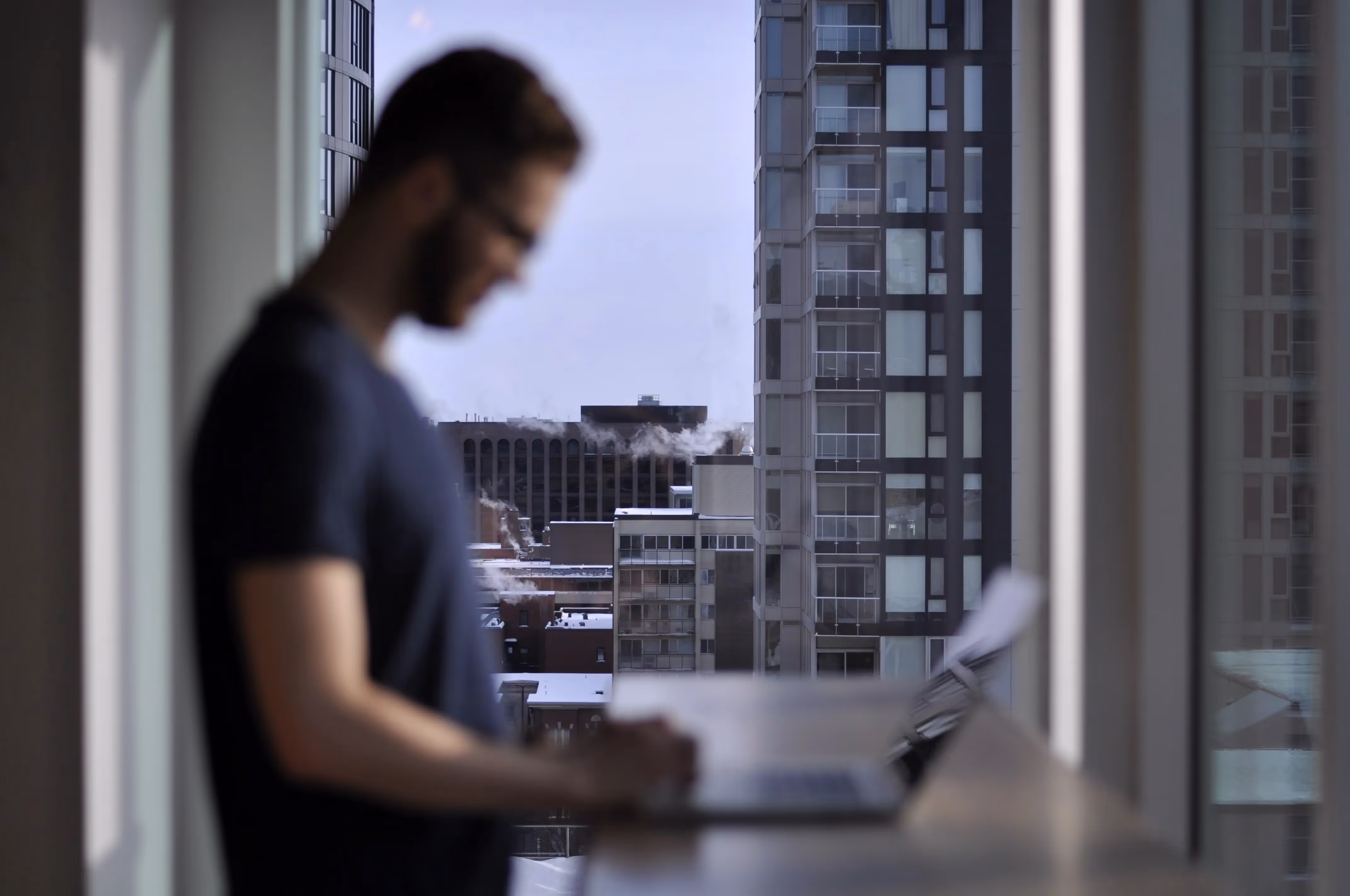A man standing in front of a window using a laptop computer