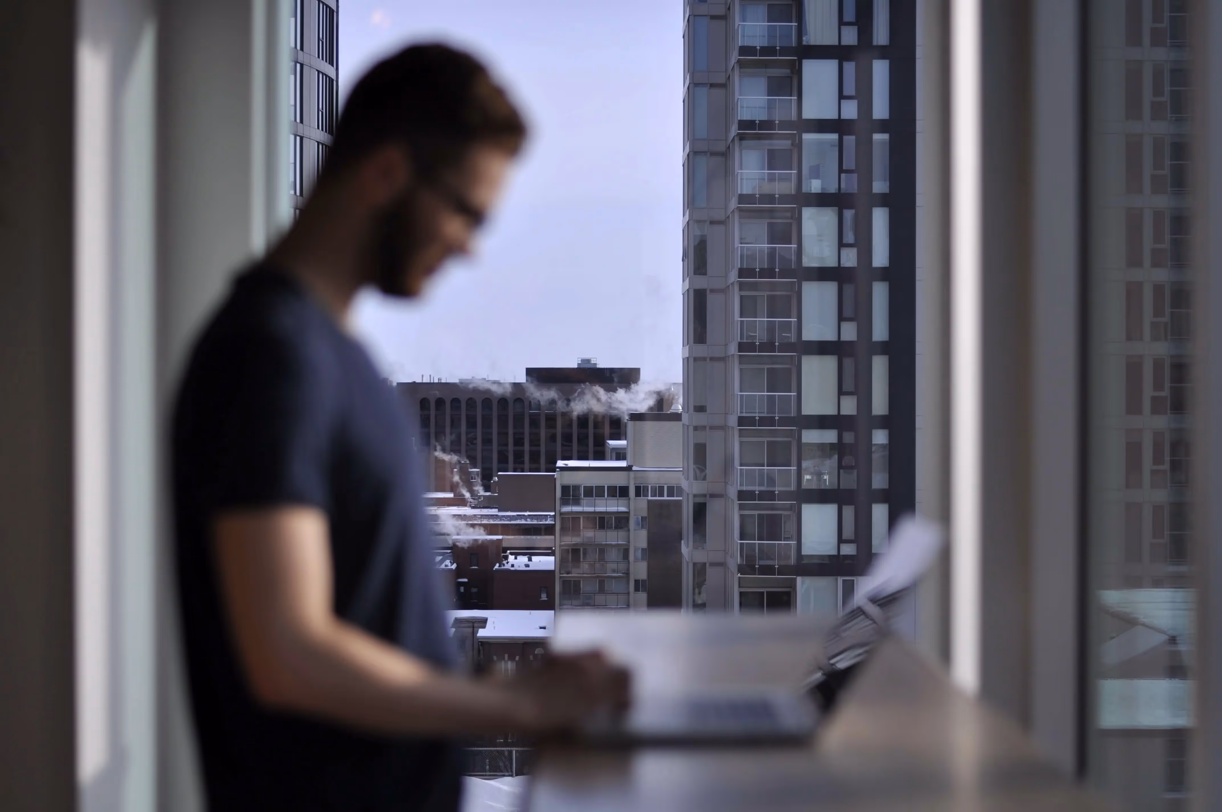 A man standing in front of a window using a laptop computer