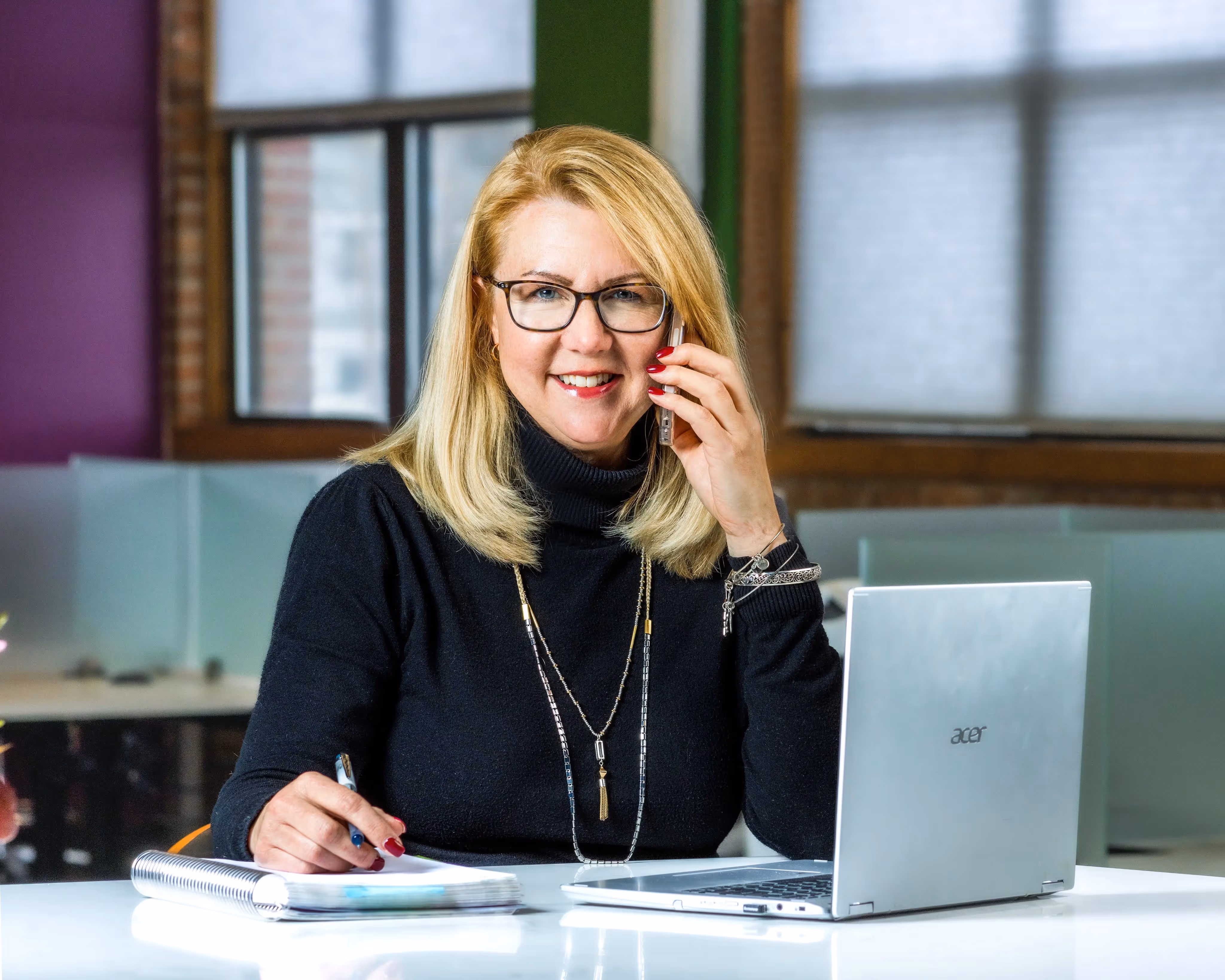 A woman sitting at a table with a laptop and cell phone