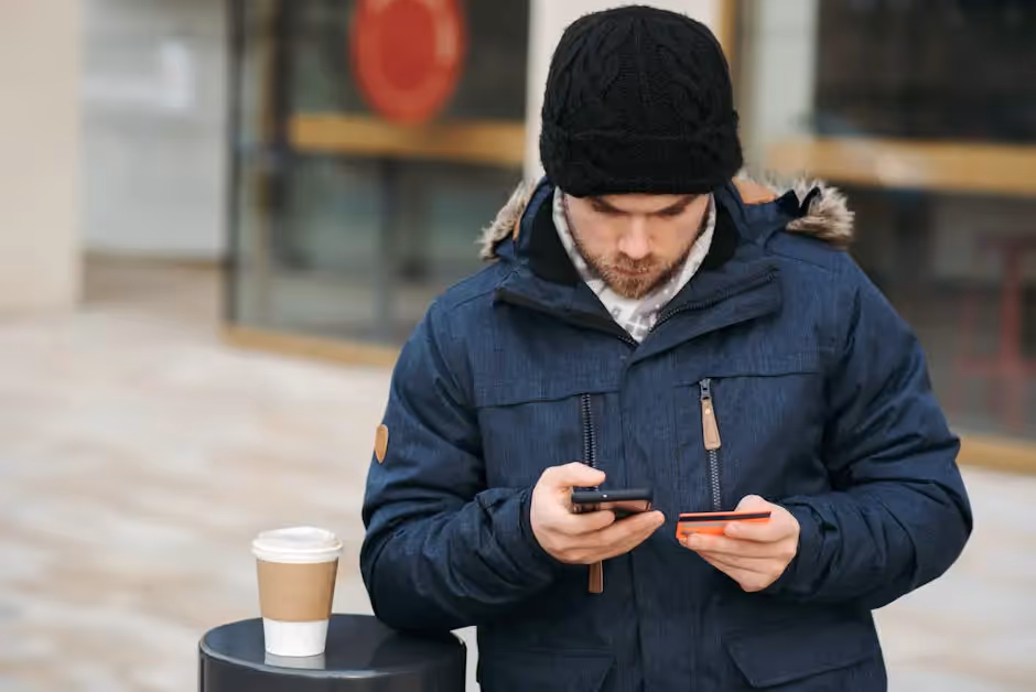 A man standing next to a cup of coffee looking at his cell phone
