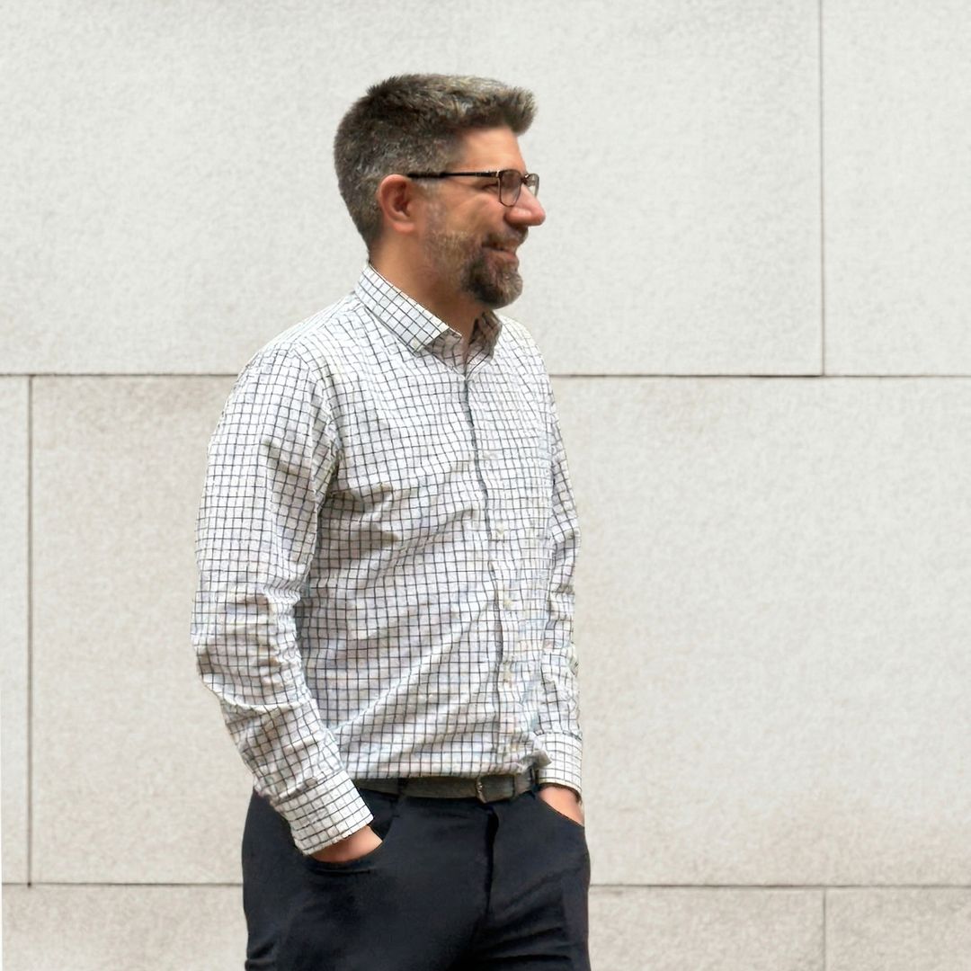 Man with glasses wearing checkered shirt standing against white wall