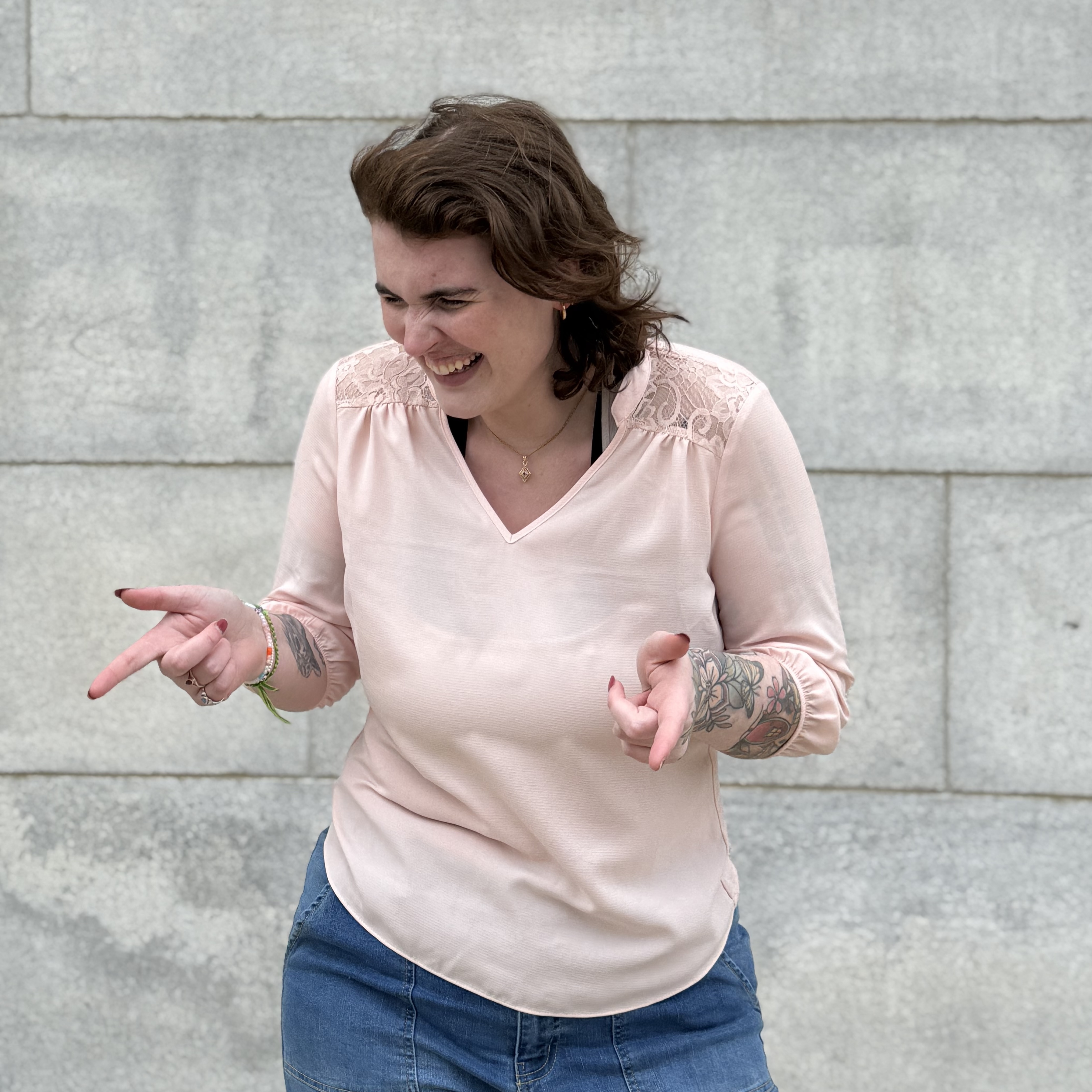 Woman with tattoos laughing while gesturing in front of concrete wall