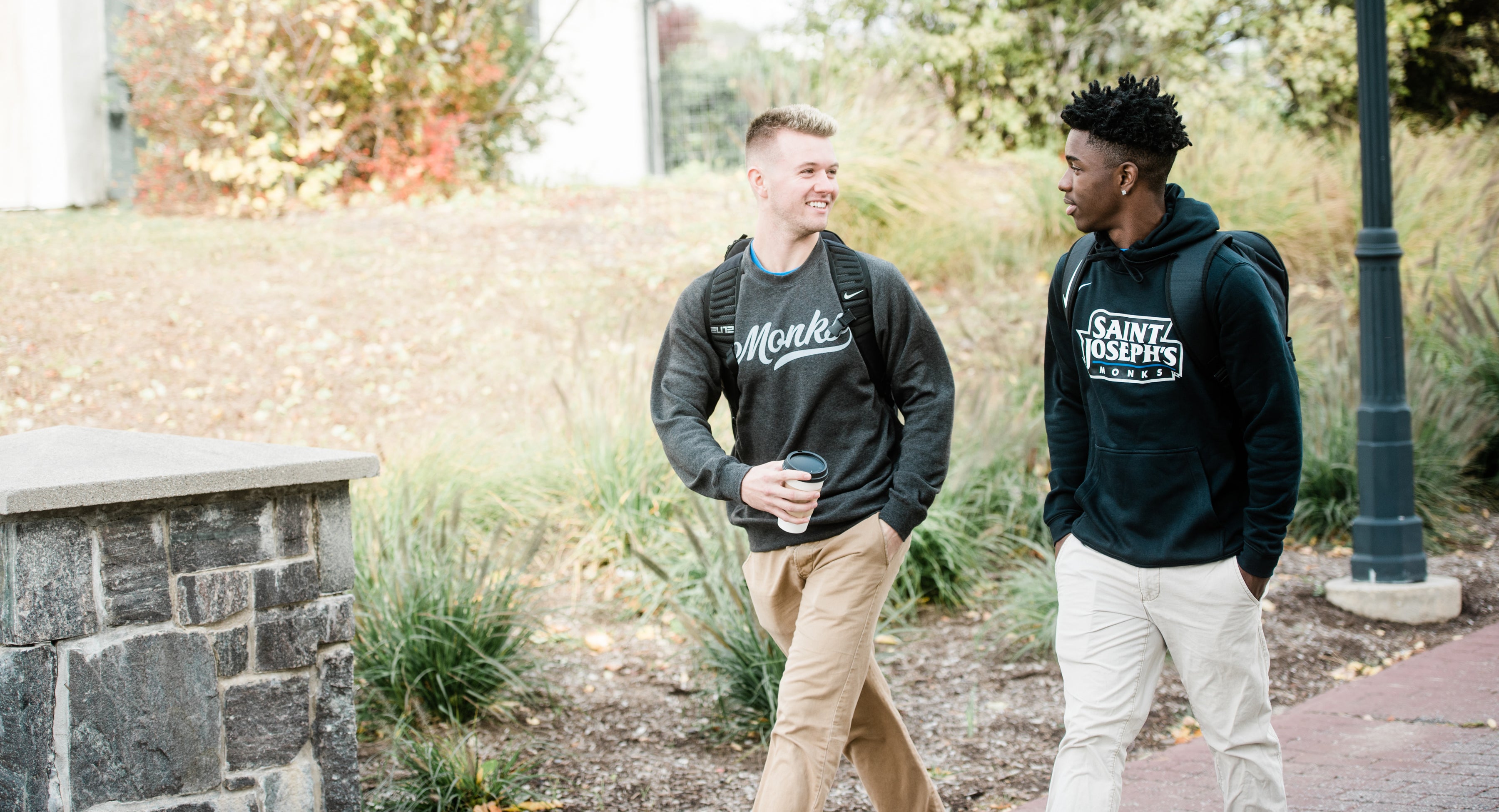 Two Saint Joseph's College students in Monks sweatshirts walking across campus in autumn