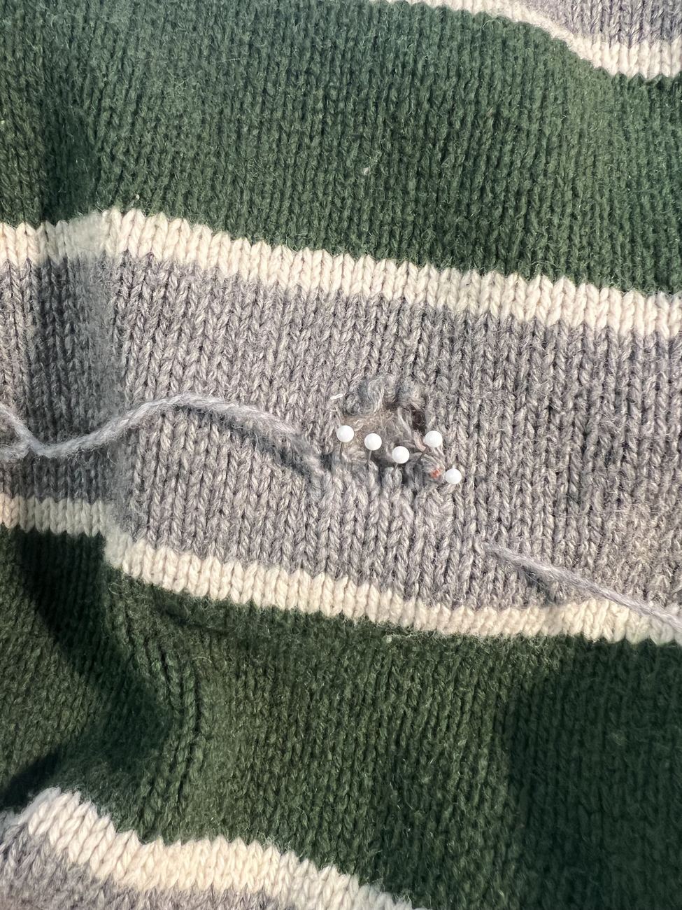 A pinned hole in the grey stripe of a striped wool sweater