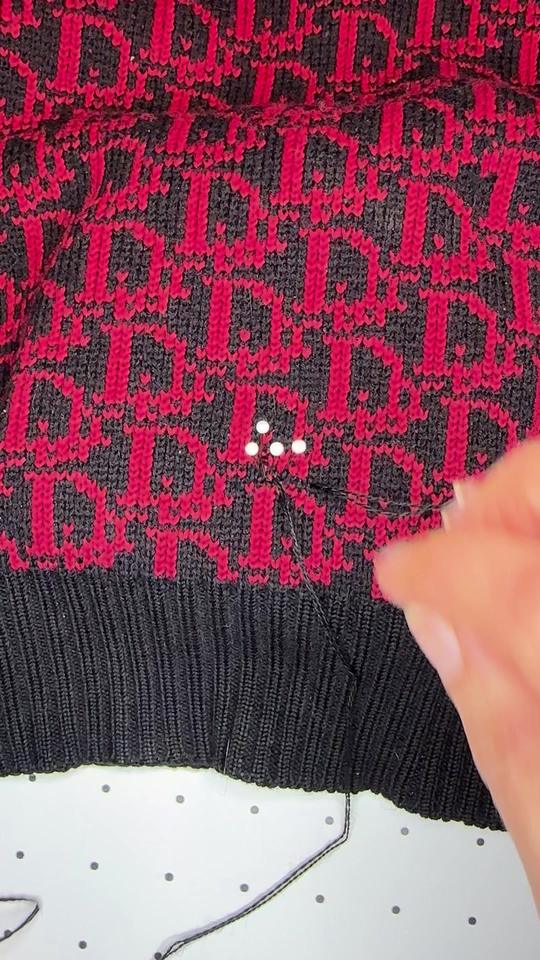 A hole by the hem of a red and black monogram knit, marked with pins