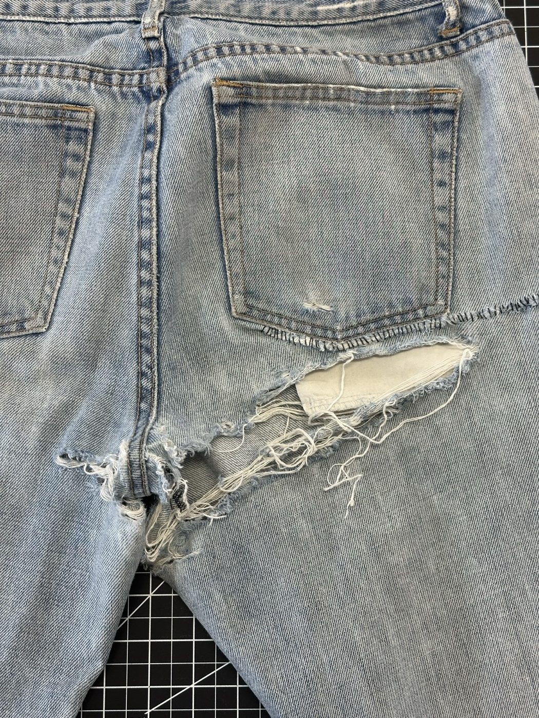 Light wash jeans torn open under the back pocket and through the seat
