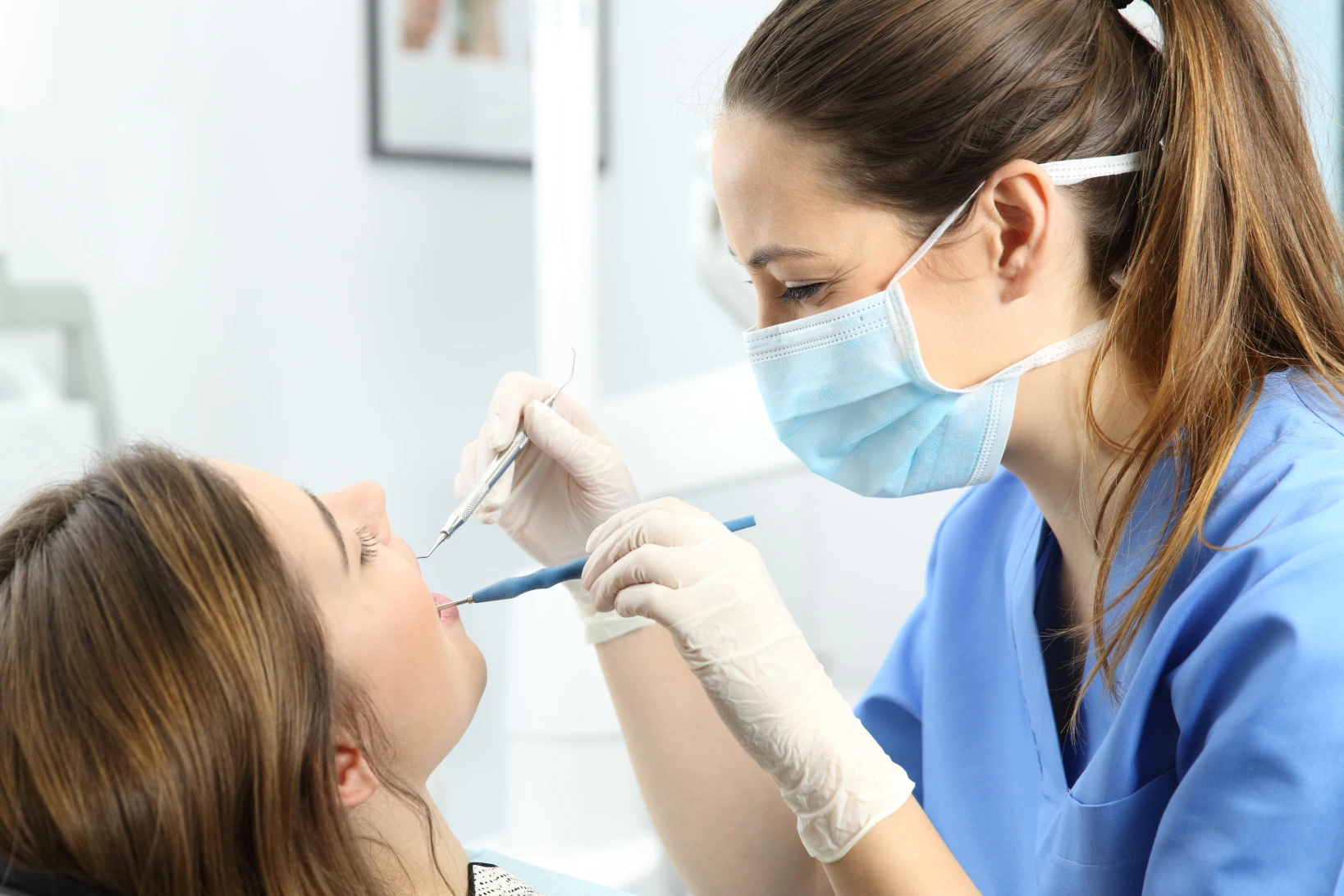Female dental hygienist with brown hair and light blue scrubs building trust with patient while cleaning her teeth