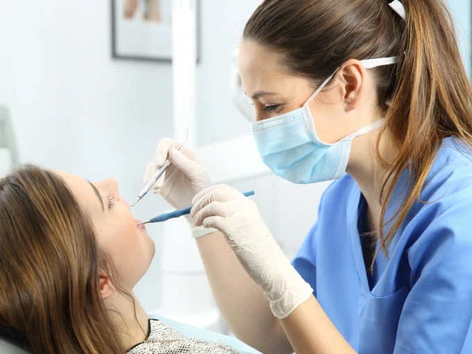 Female dental hygienist with brown hair and light blue scrubs building trust with patient while cleaning her teeth