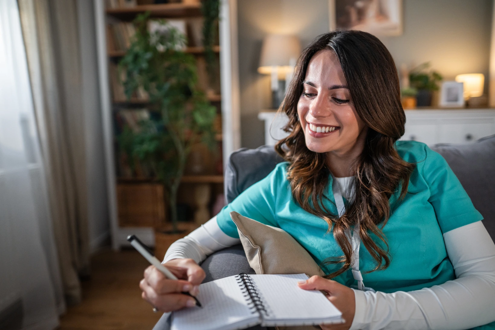 Female nurse in green scrubs sitting on a couch with planner open while conducting long-term goal setting for LPNs