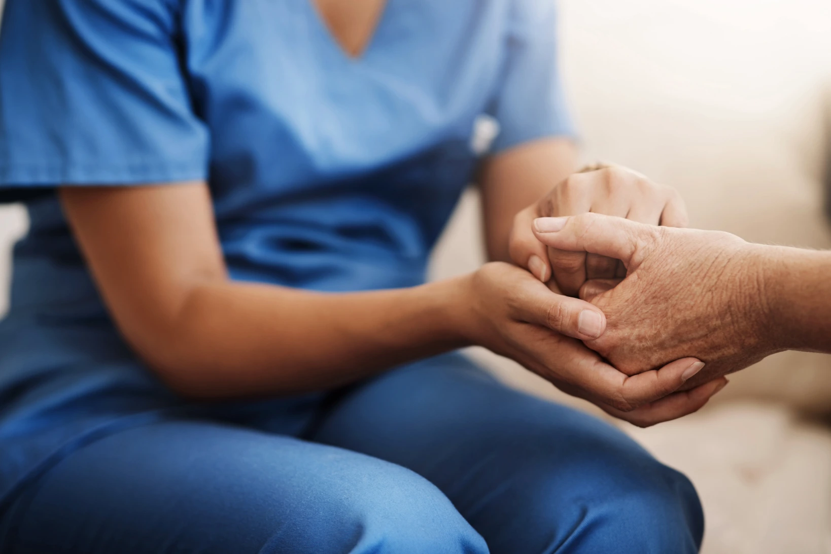 Nurse in blue scrubs holding hands with and advocating for a patient
