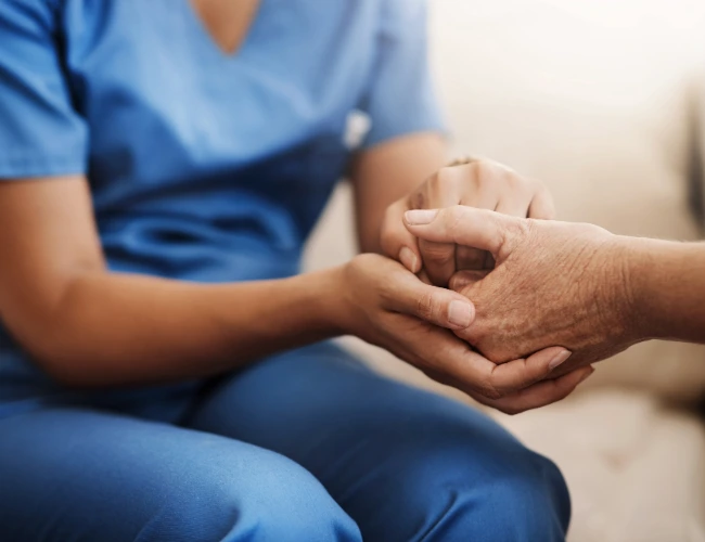 Nurse in blue scrubs holding hands with and advocating for a patient