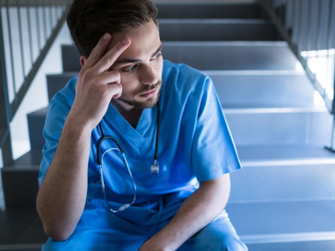 Male nurse sitting on stairs with head in hands trying to cope with the emotional toll of nursing