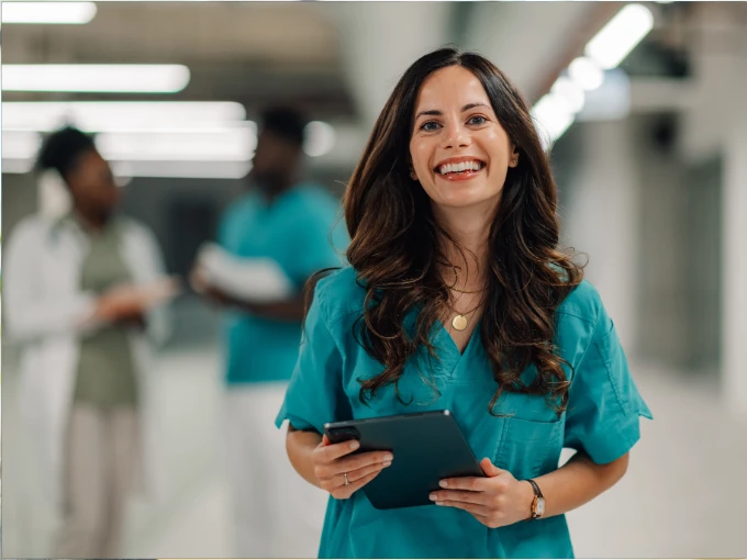 Registered nurse in scrubs holding a tablet in a hospital hallway, representing RN license transfer and nursing career mobility
