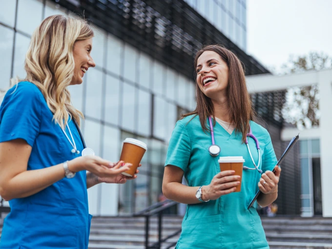 Two nurses chatting about online nursing school options outside of their hospital