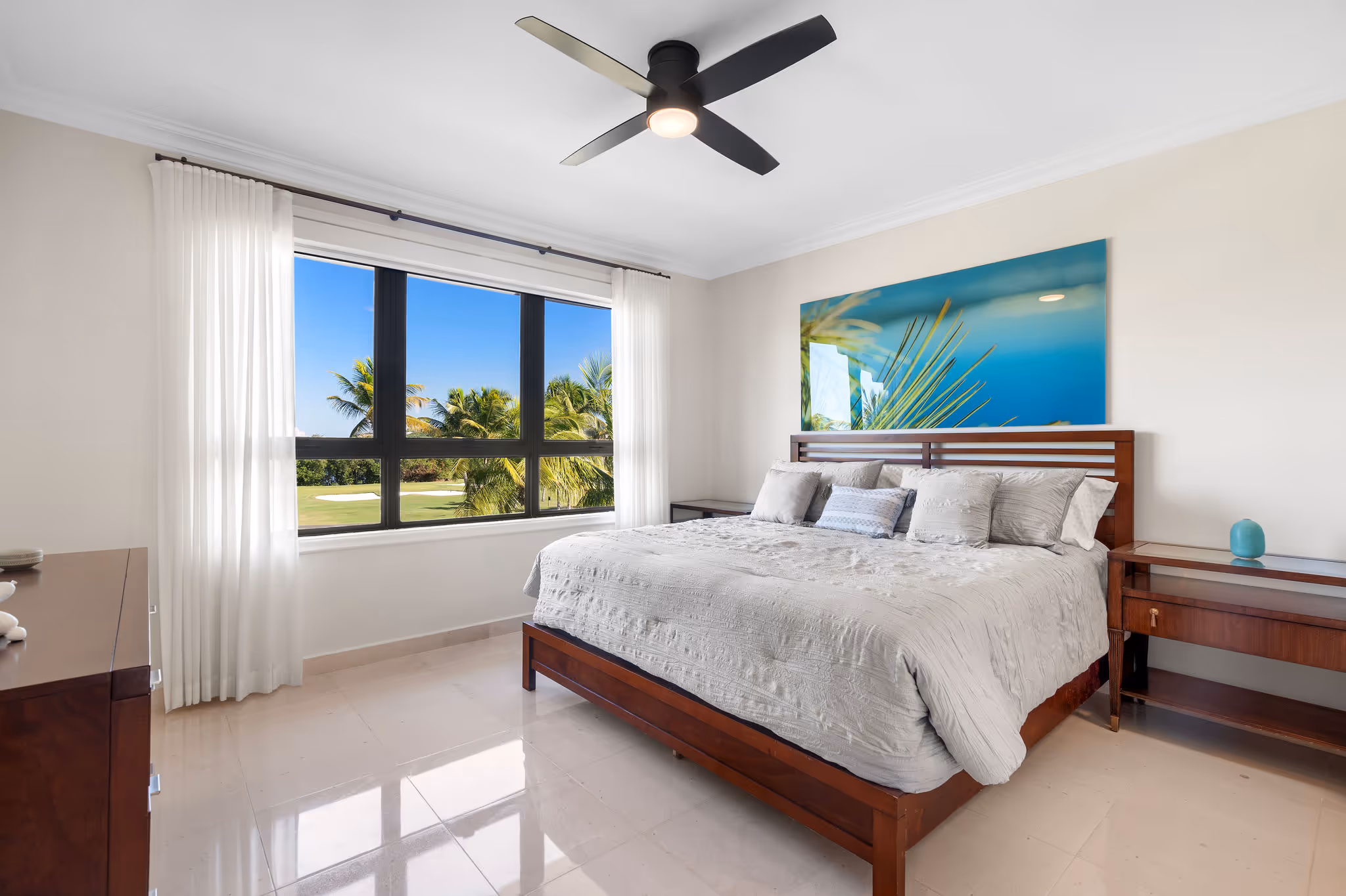 21. Country Club Villas F302 Image 21: Serene guest bedroom with a king-sized bed, modern ceiling fan, and large windows that offer picturesque views of the tropical landscape.