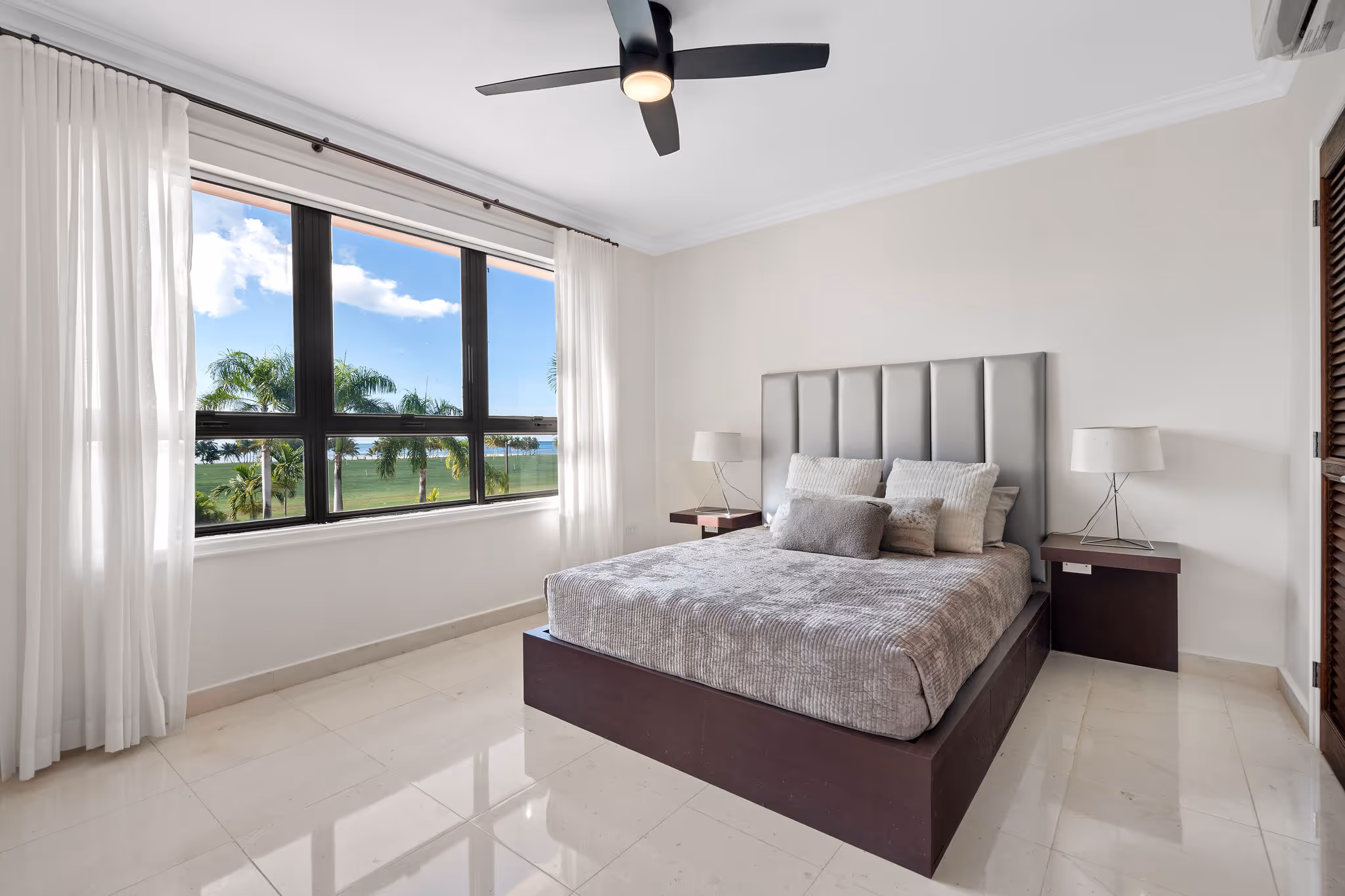 23. Country Club Villas F302 Image 23: Another stylish guest bedroom with a full-sized bed, modern ceiling fan, contemporary furnishings, elegant neutral tones, and tropical golf course scenery.