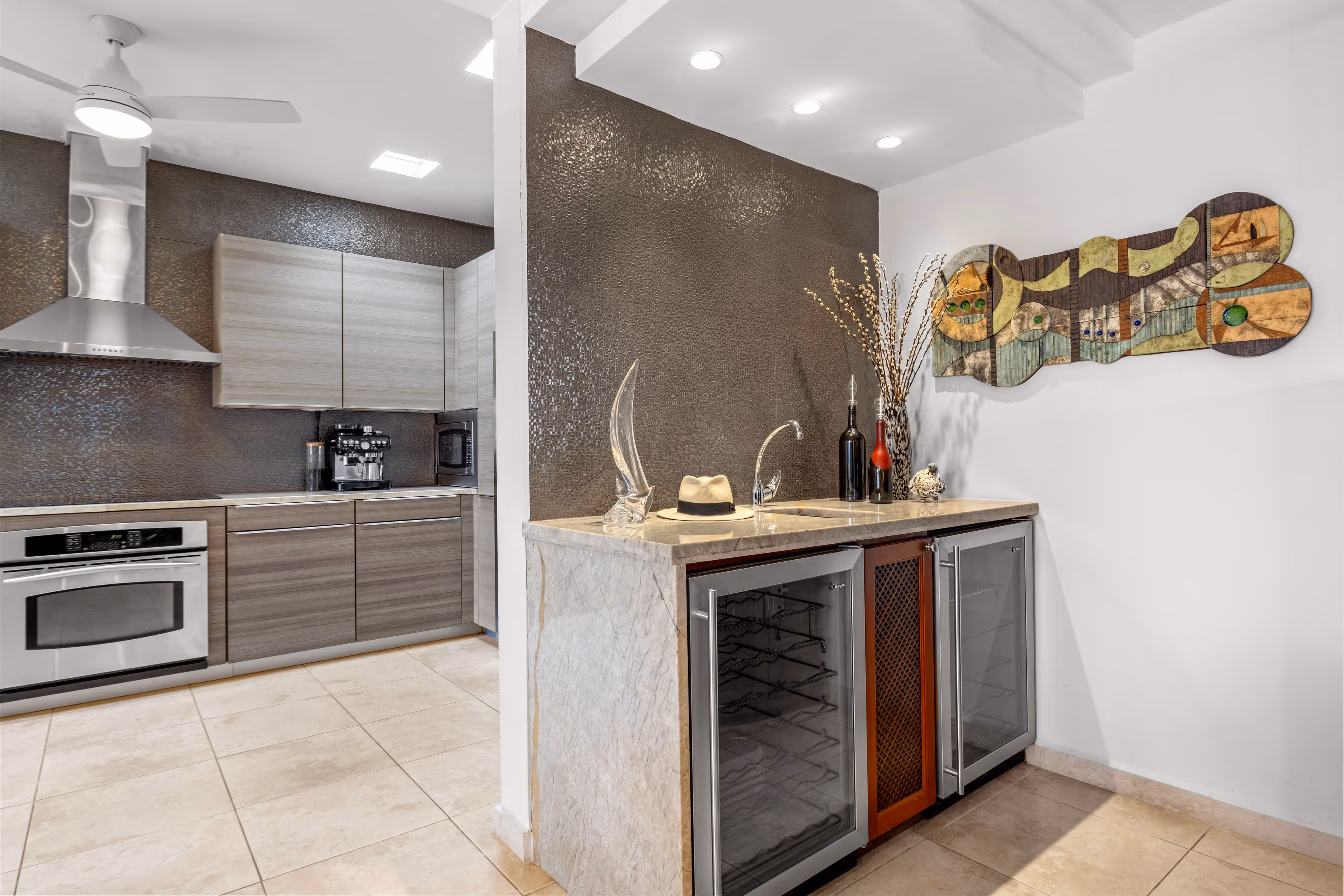 Sophisticated wet bar area with marble countertops and custom cabinetry in a modern Villas Reales residence, adjacent to the gourmet kitchen.