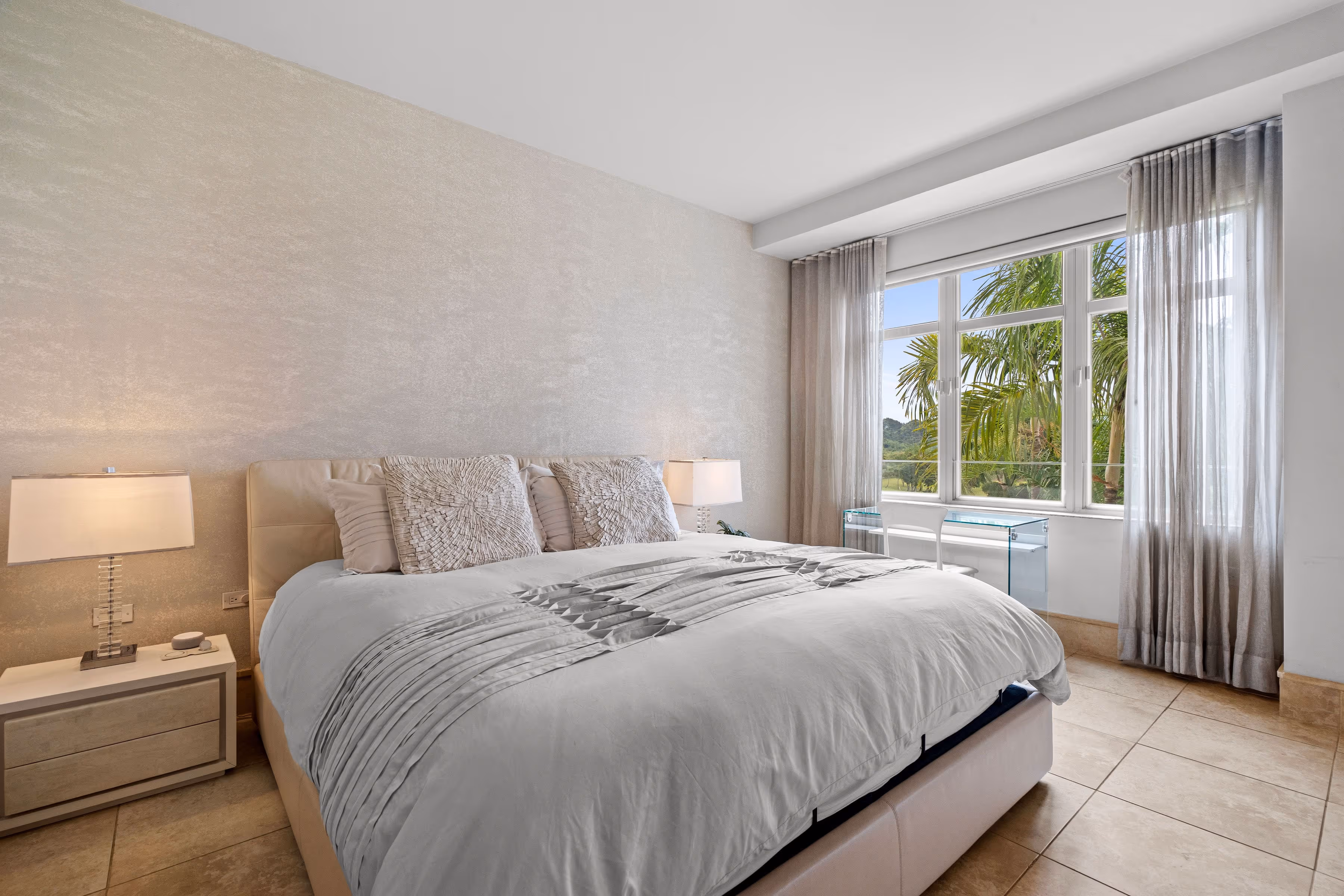 Elegant bedroom with luxurious bedding and large windows showcasing tropical views at Plantation Village, Dorado Beach Resort