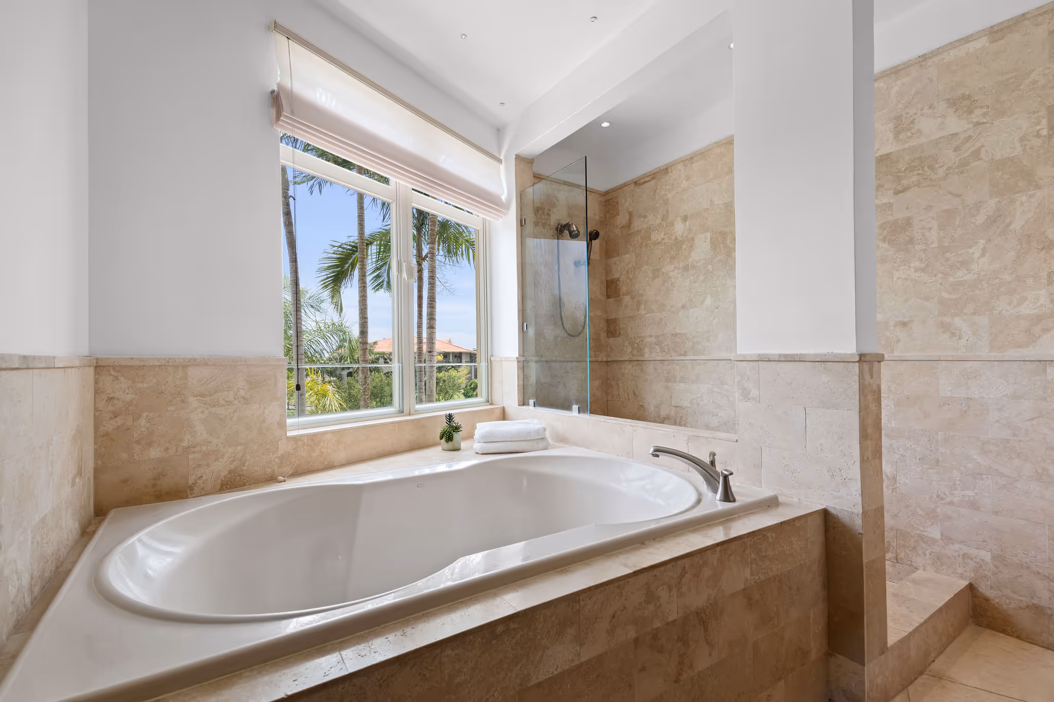 Spa-like soaking tub and glass-enclosed shower with natural stone finishes in Dorado Beach Resort master bathroom