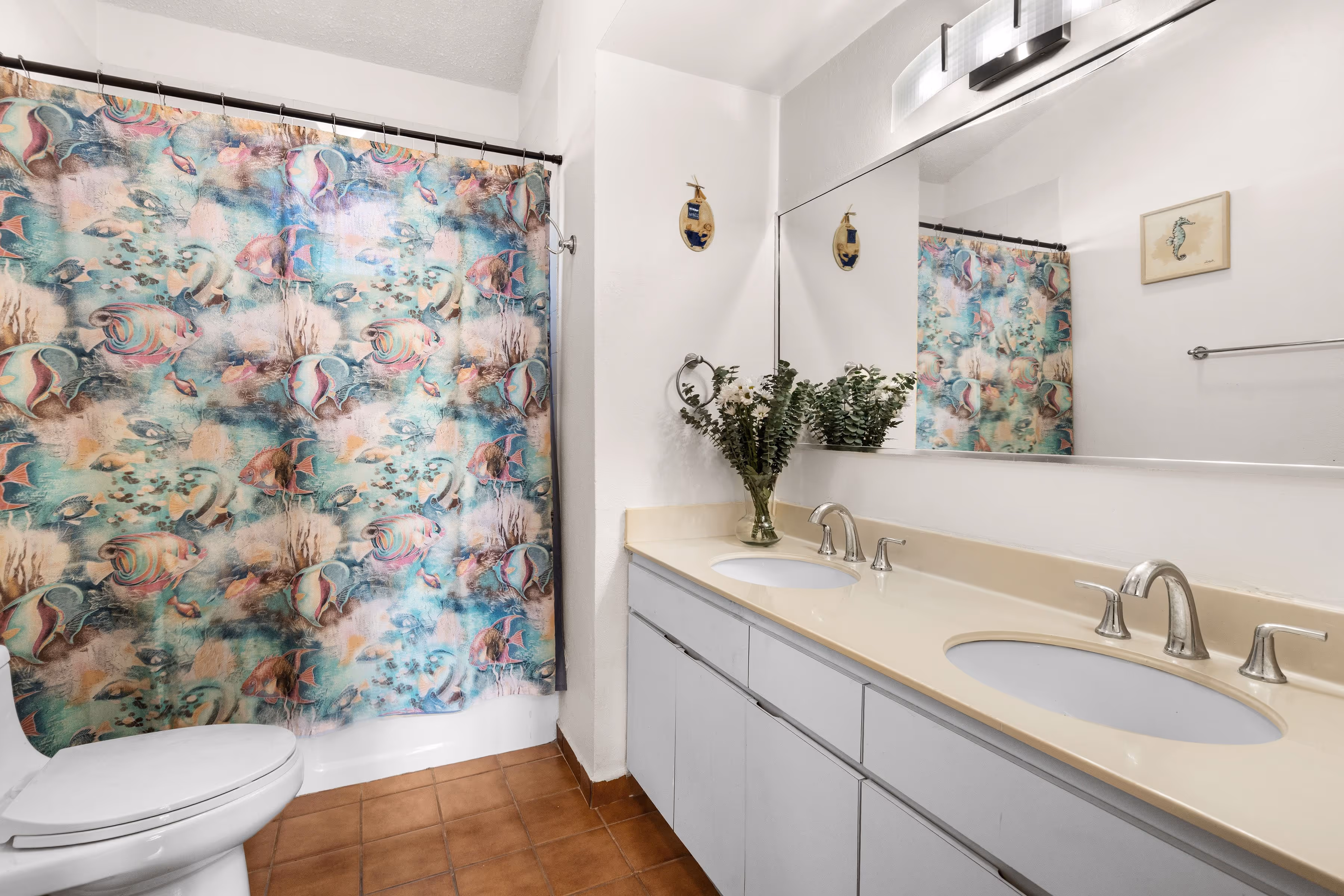 Full bathroom with double-sink vanity, large wall mirror, modern fixtures, and colorful tropical fish shower curtain inside a second-floor Fairlakes Village condo in Palmas del Mar.