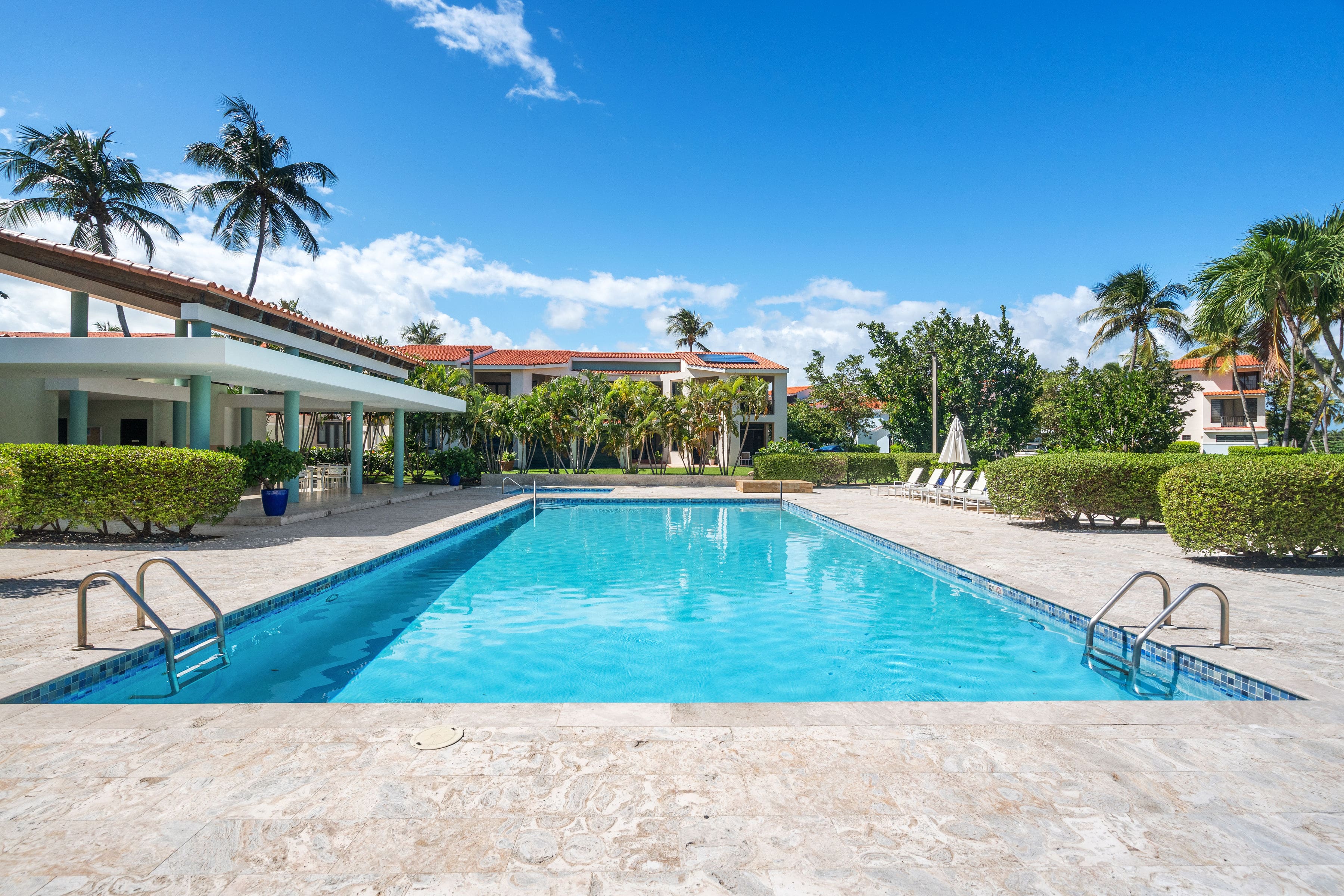 Community pool framed by tropical landscaping, sun loungers, and the open-air gazebo pavilion at Fairlakes Village in Palmas del Mar.