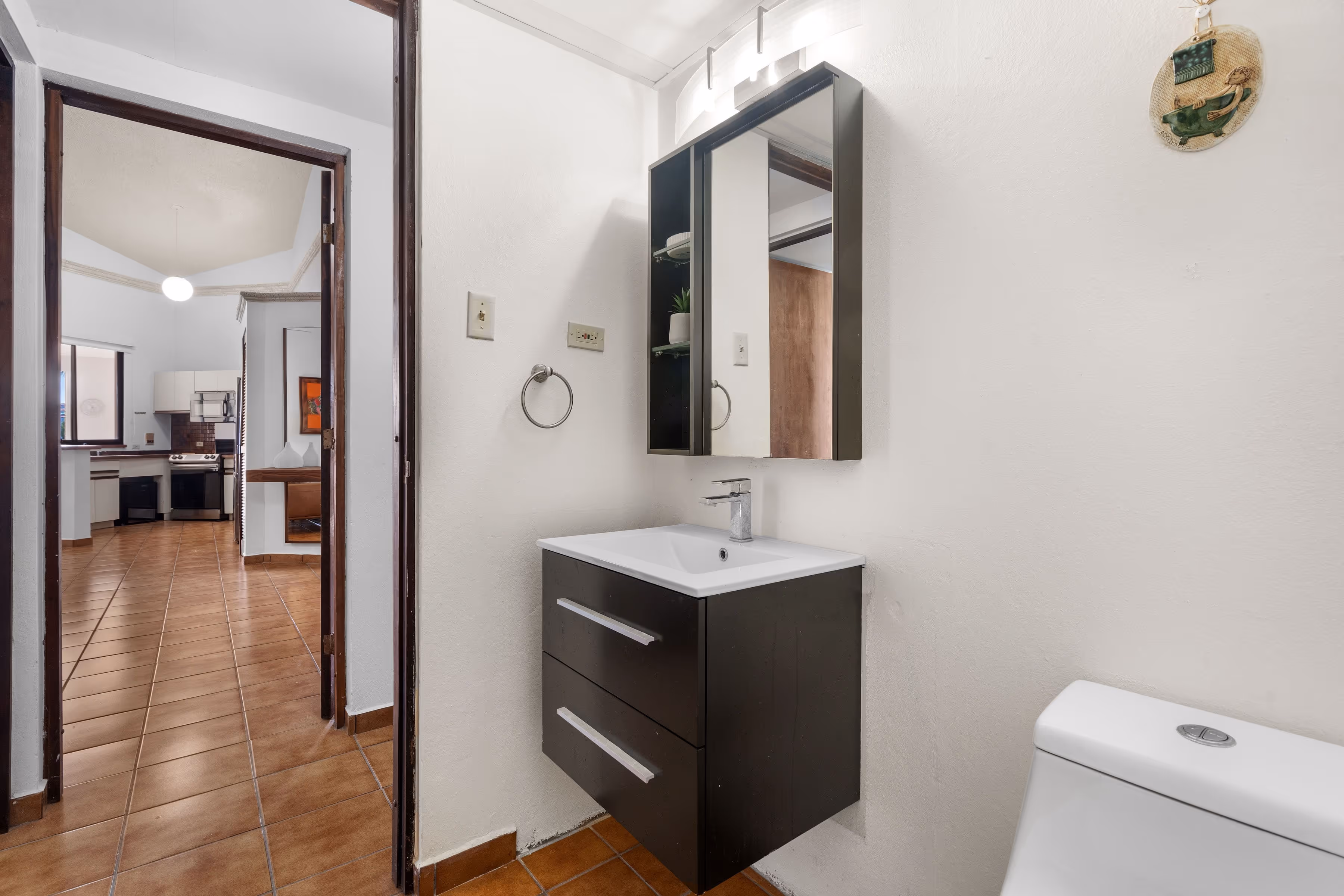 Secondary bathroom with floating vanity, modern lighting, and direct hallway access leading toward the open living area and kitchen in Fairlakes Village.