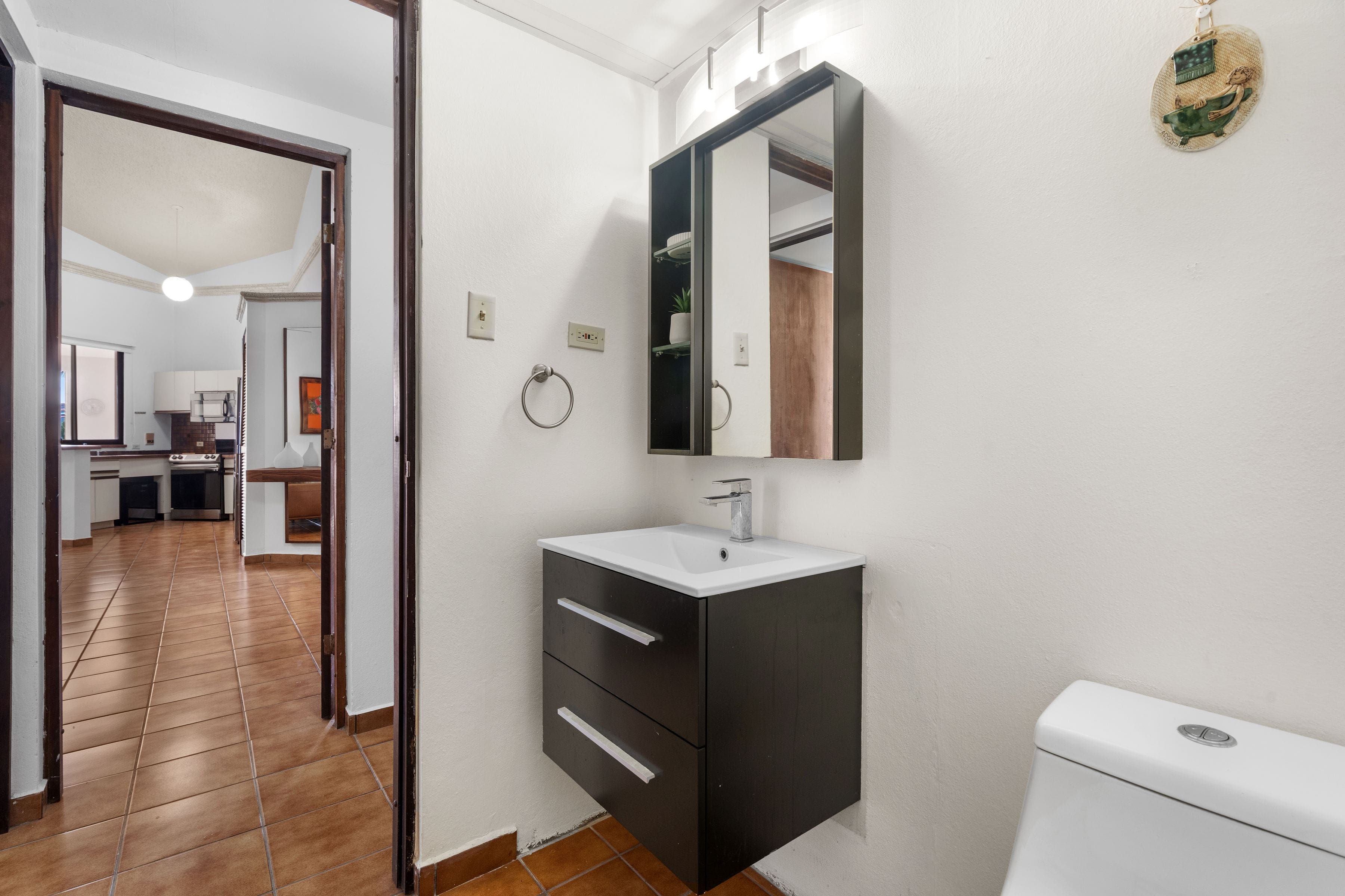 Secondary bathroom with floating vanity, modern lighting, and direct hallway access leading toward the open living area and kitchen in Fairlakes Village.