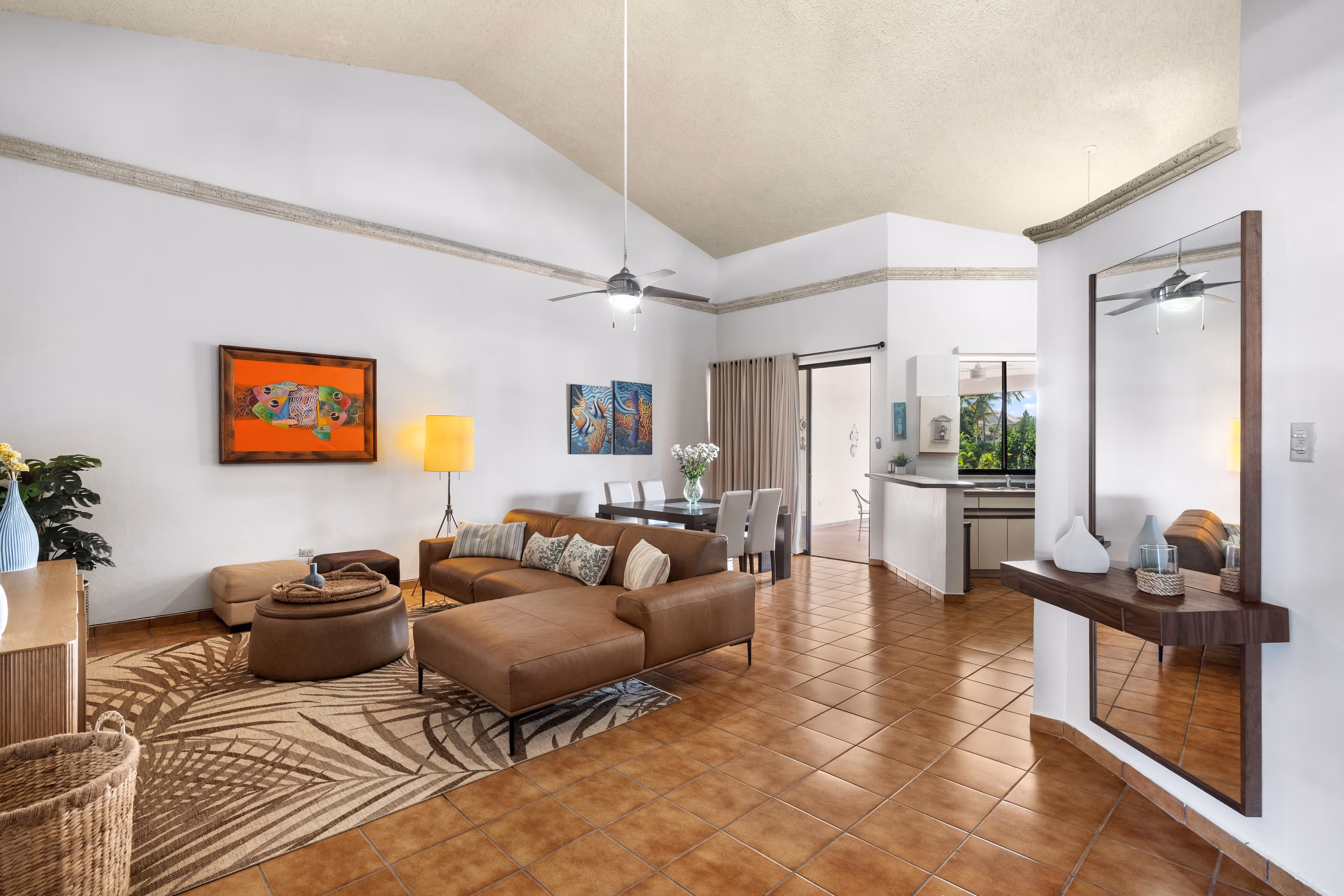 Open-concept living and dining room with high ceilings, natural light, leather sectional sofa, warm terracotta flooring, and furnished interiors in a second-floor Fairlakes Village condo in Palmas del Mar.