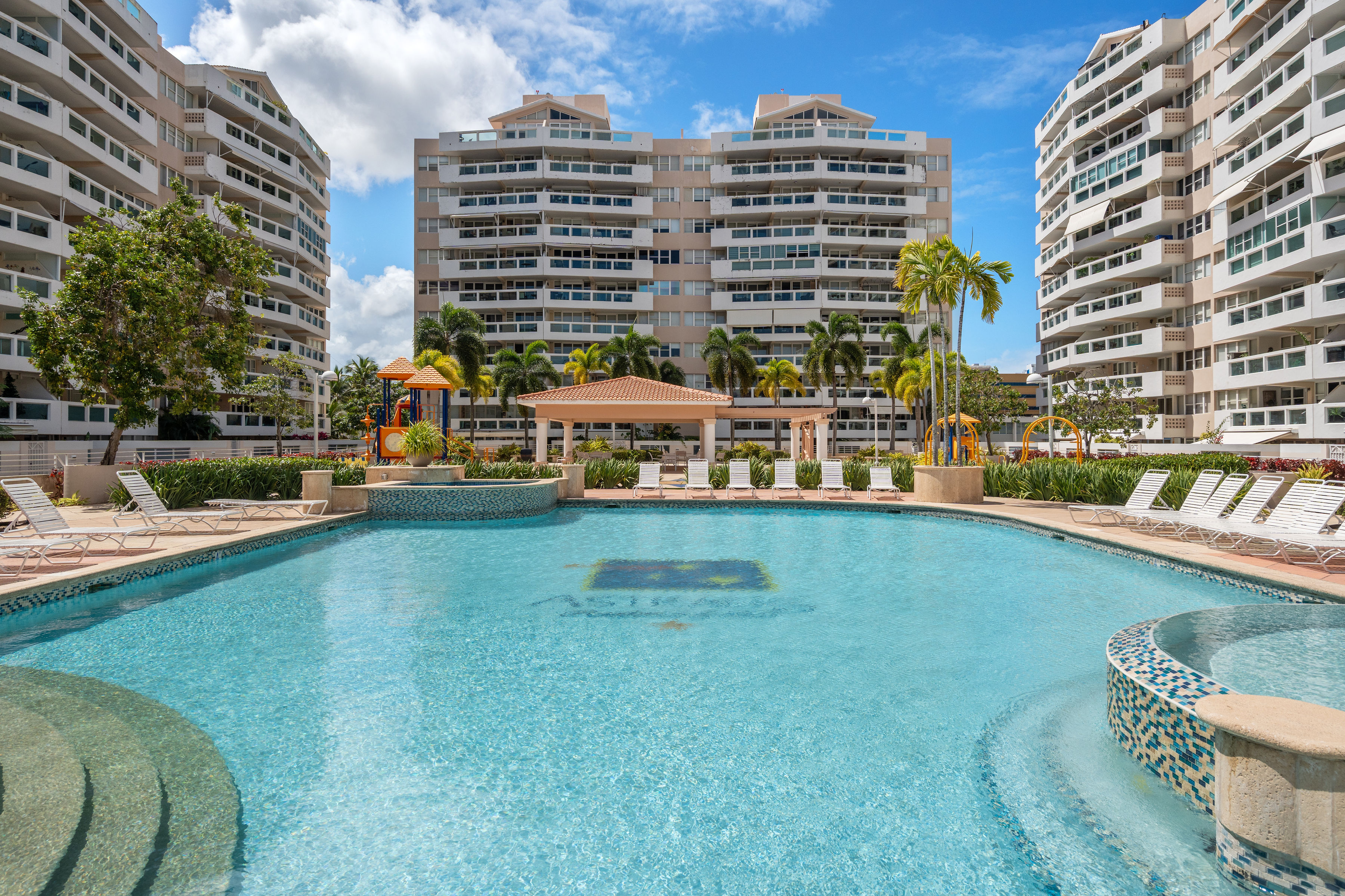 Astralis Isla Verde resort-style pool with sun deck lounge chairs and landscaped surroundings