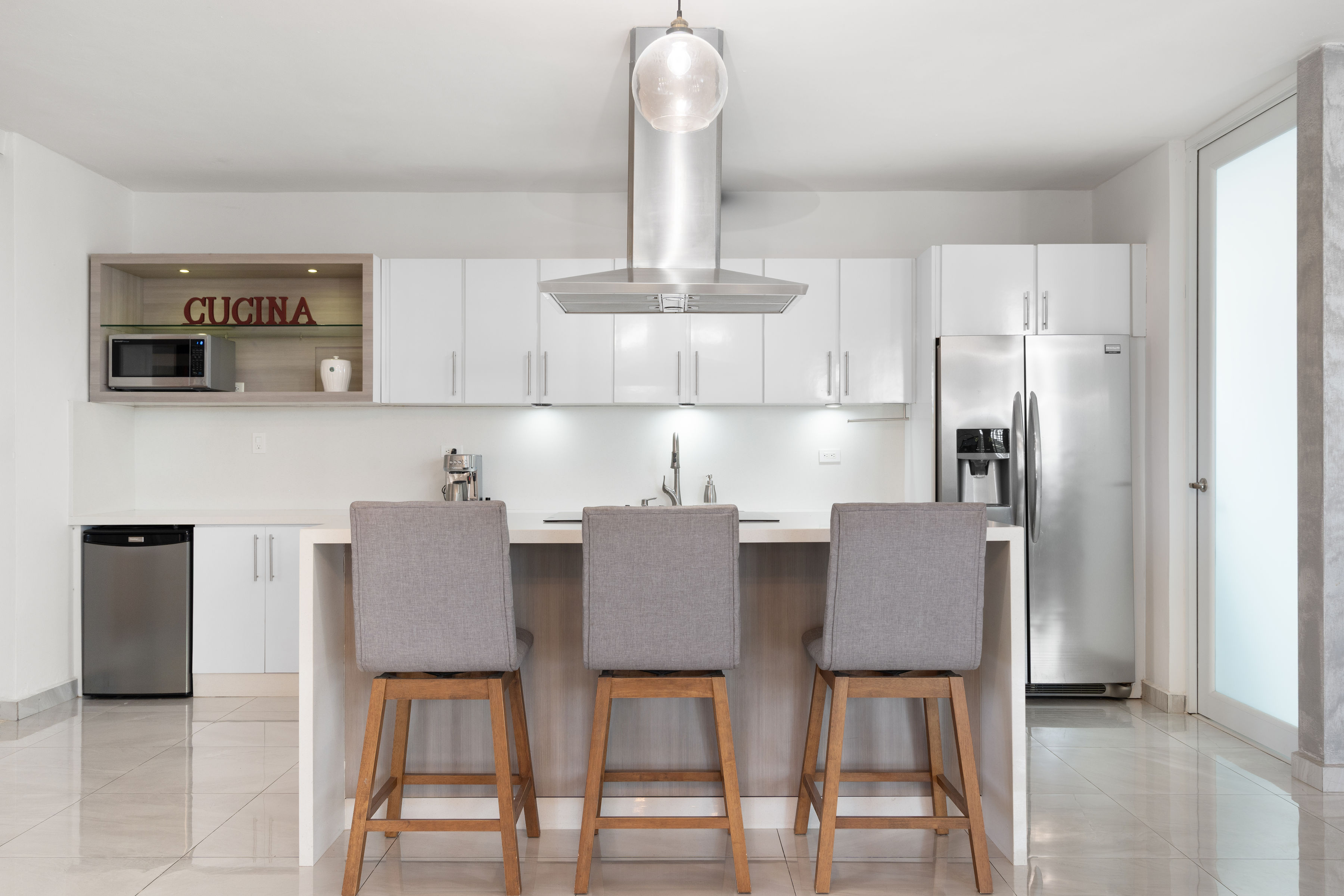 Modern white kitchen with island seating and stainless steel appliances in San Juan residence