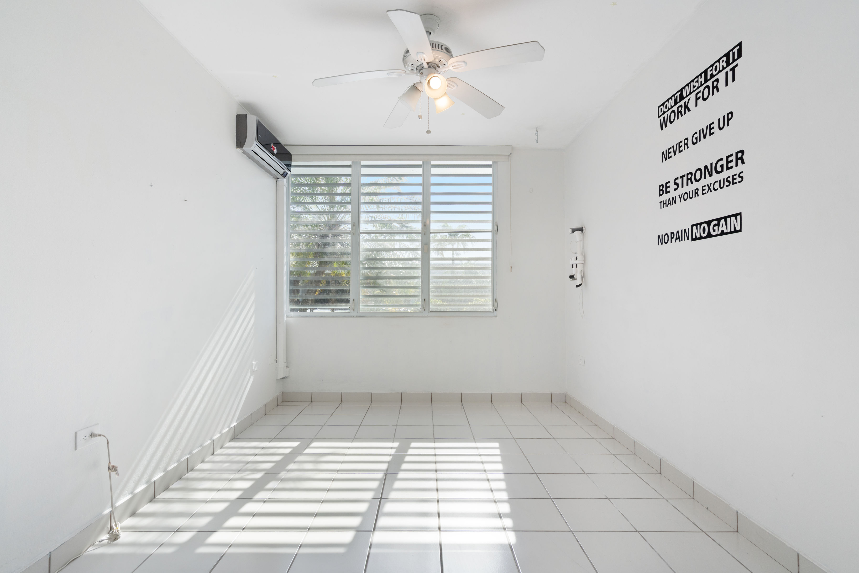 Empty flexible room with natural light, window views and wall quote in Villanova residence