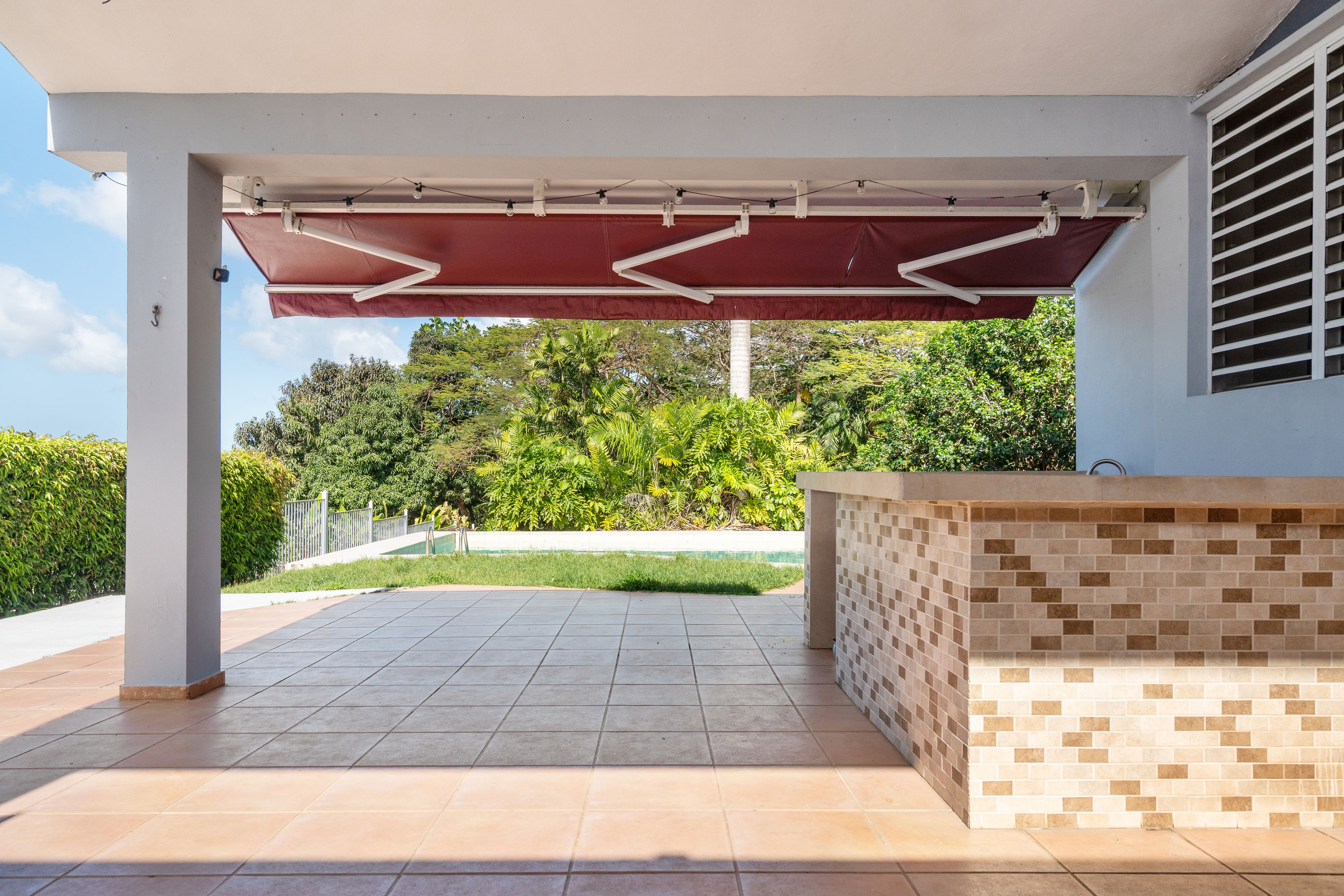 Covered outdoor terrace with bar area overlooking backyard and pool in San Juan residence