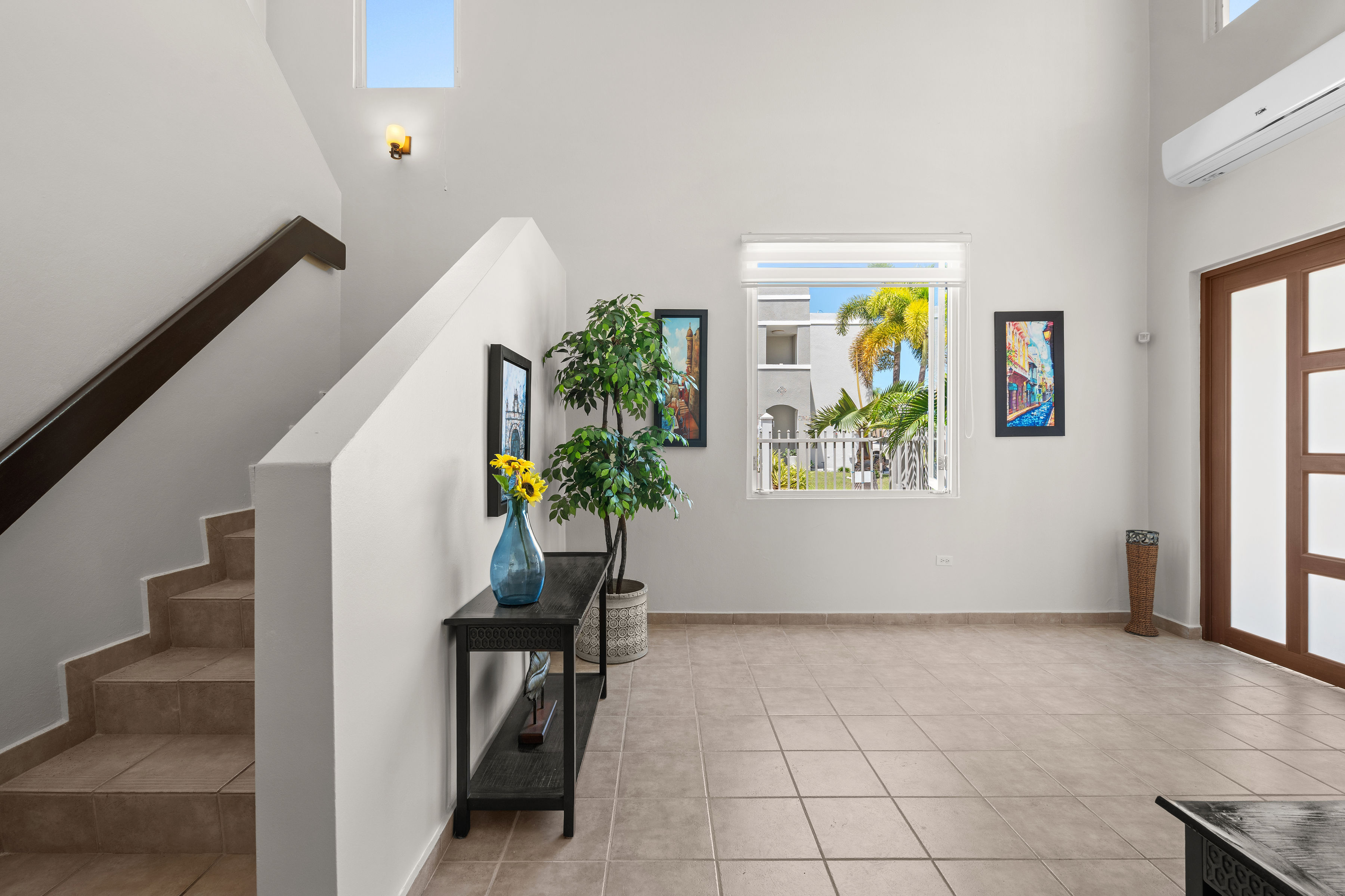 Bright entrance area with high ceilings, large window, and staircase detail creating an open and welcoming interior space in Cielo Dorado Village residence
