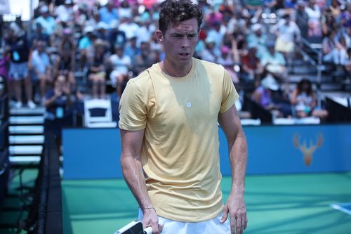Tennis player in a yellow shirt on a court with blurred spectators in the background.