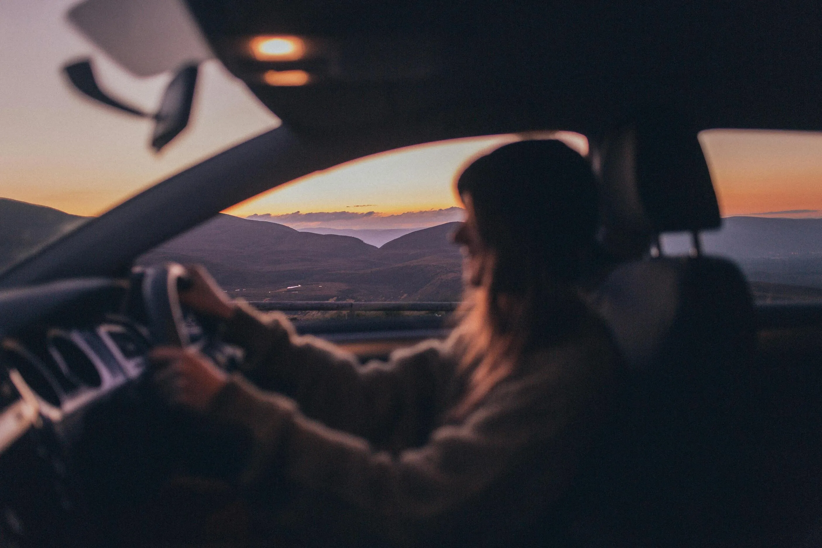 A woman driving a car with mountains in the background.