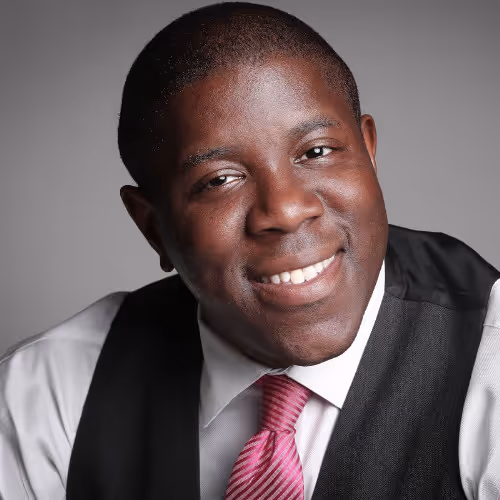 Smiling man wearing a white shirt, pink striped tie, and black vest against a gray background.