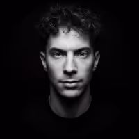 Black and white portrait of a young man with curly hair against a dark background.