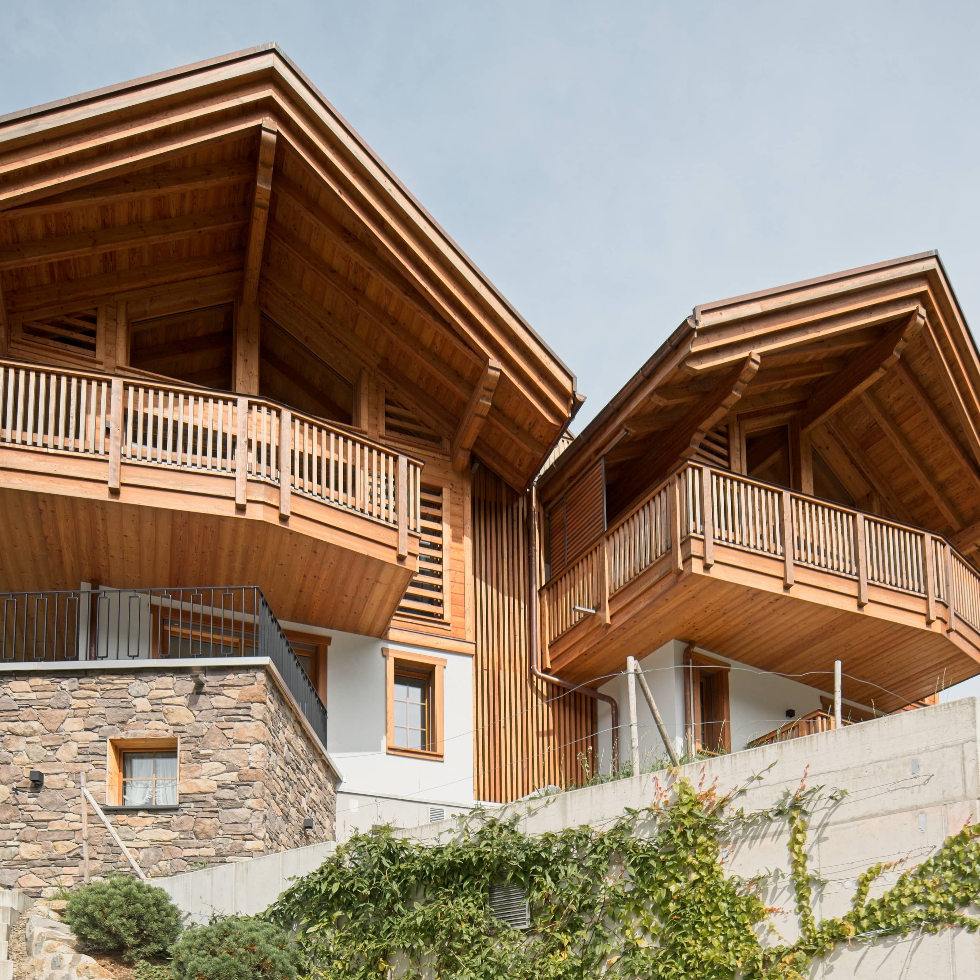 Modernes Chalet mit Holzfassade, zwei Balkonen und Steinmauer im Vordergrund.