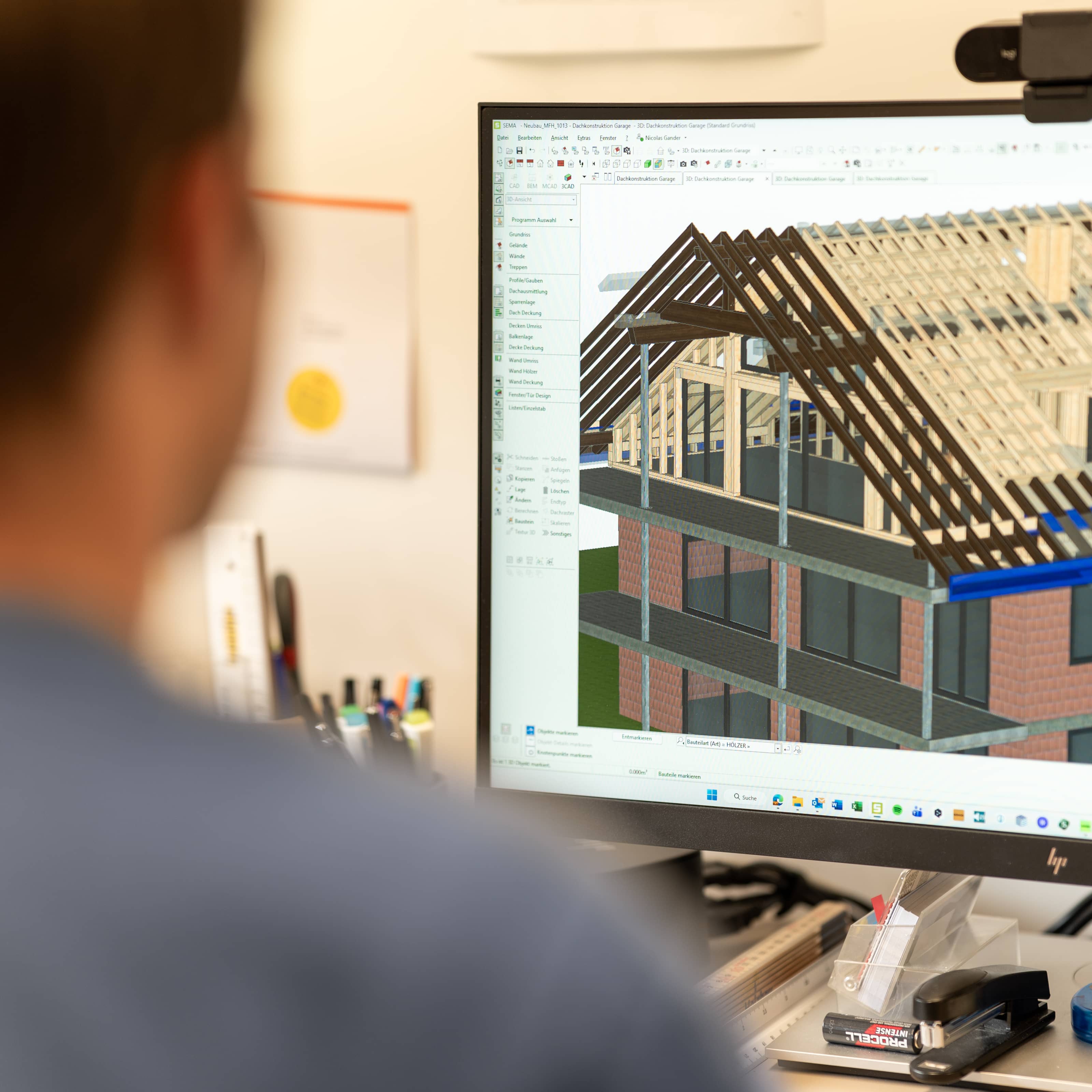 Person betrachtet 3D-Architekturmodell eines Hauses mit Dachkonstruktion auf einem Computerbildschirm.