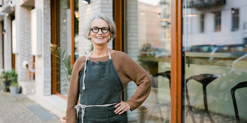 Senior woman in front of a coffee shop smiling after receiving a Bizcap loan