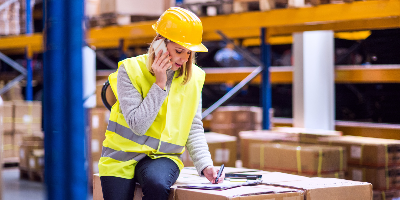 Female transport worker in warehouse on phone 