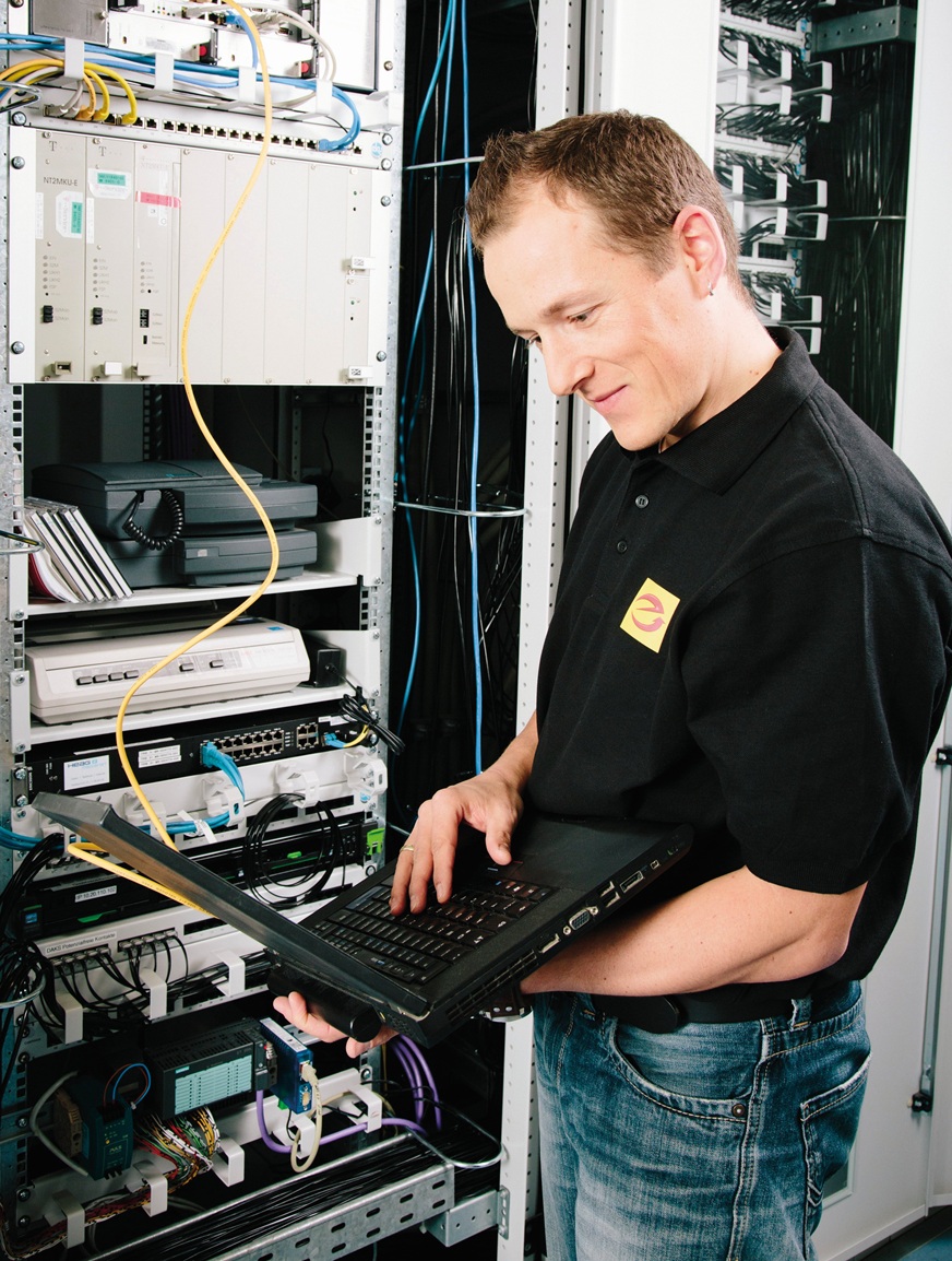Fachmann steht mit Laptop vor Serverschrank.