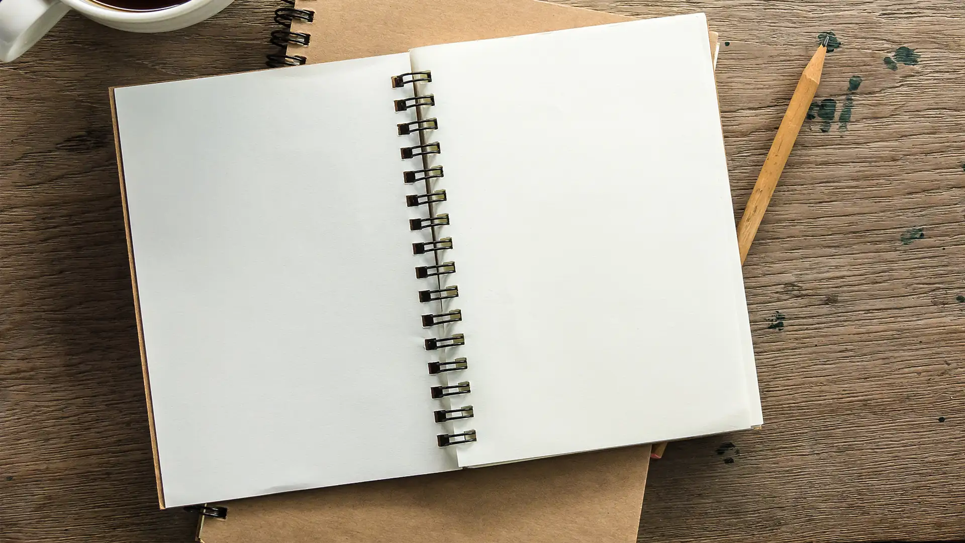 Leeres, aufgeschlagenes Spiralnotizbuch auf Holztisch mit Bleistift und Tasse Kaffee